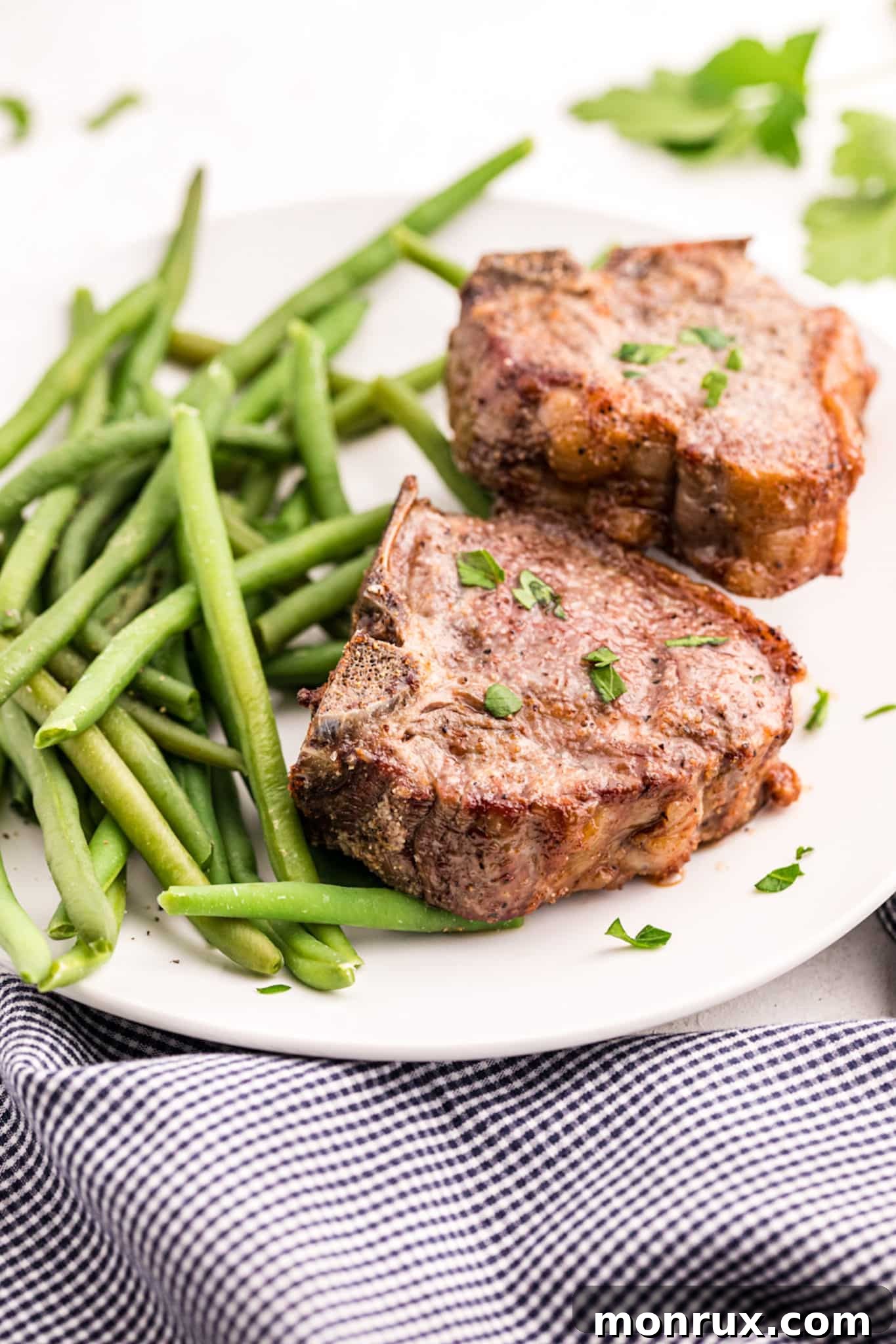 Cooked lamb chops on a white platter with cooked green beans.