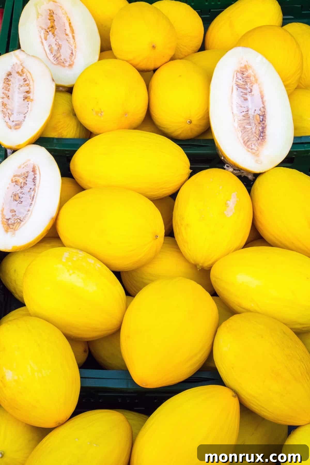 A pile of canary melons with 2 cut open.