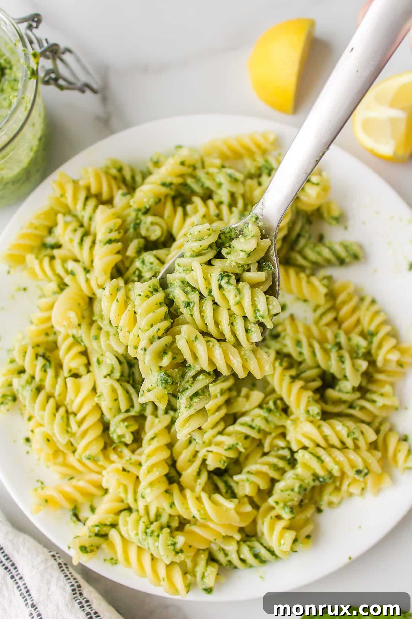 A beautifully presented bowl of dairy-free pesto pasta, garnished with fresh basil leaves and ready to be enjoyed. A spoon rests in the bowl, inviting a taste.