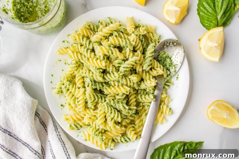 A plate of freshly prepared vegan pesto pasta served with a spoon, highlighting its vibrant green sauce and inviting presentation.