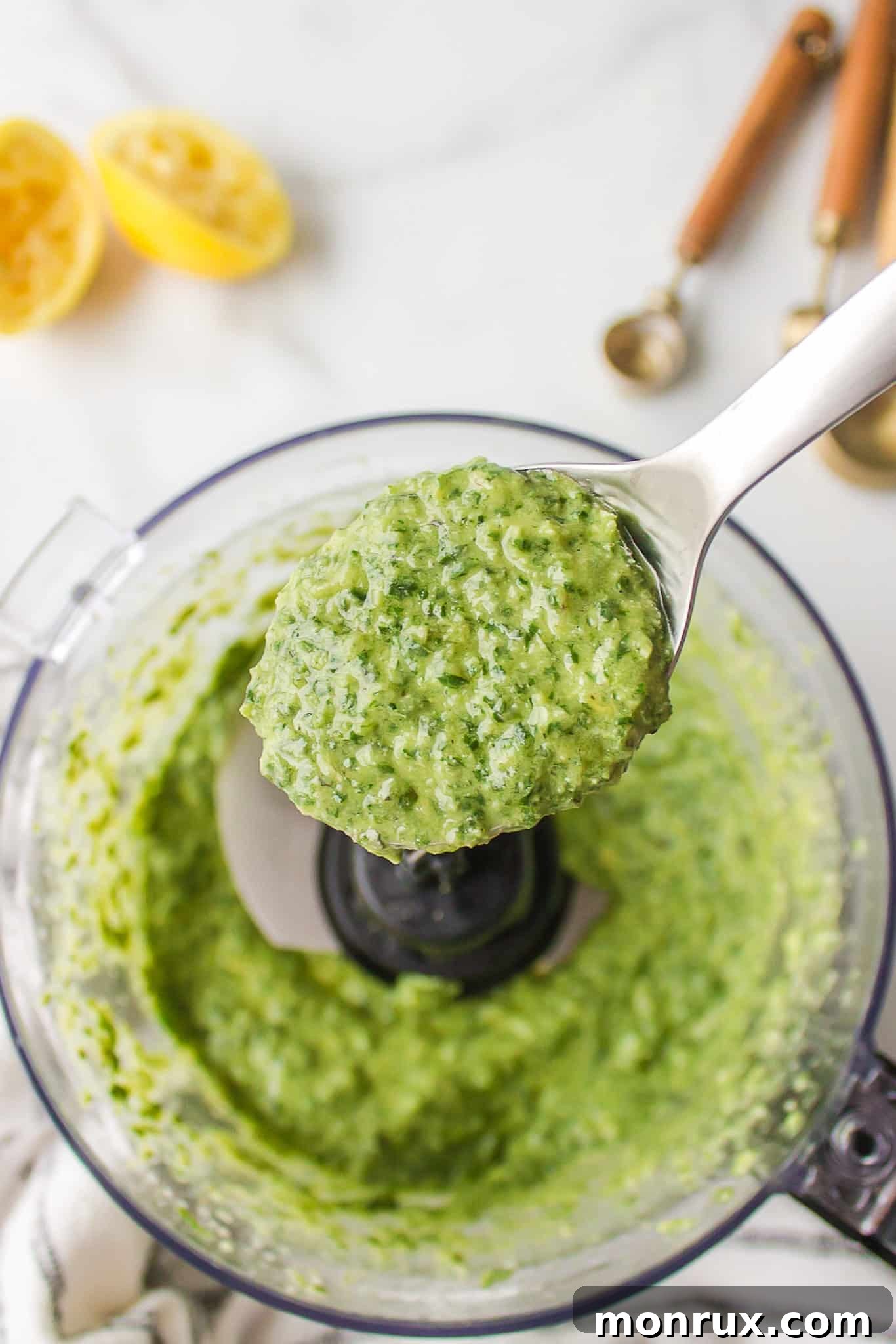 A close-up of vibrant dairy-free pesto sauce, freshly made in a food processor, scooped onto a spoon to show its smooth and rich texture.