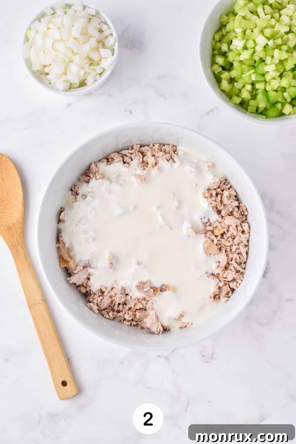 A generous portion of shredded chicken resting in a bowl, with a rich, creamy dressing poured over it, ready for mixing.