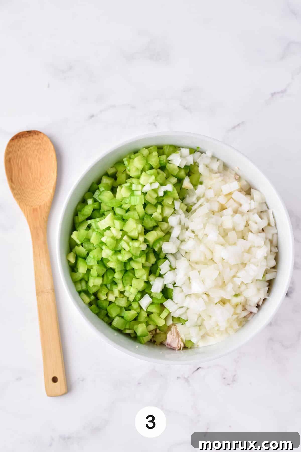 A vibrant bowl containing finely chopped celery and diced white onion, prepared and ready to be added to the chicken salad mixture for crunch and flavor.