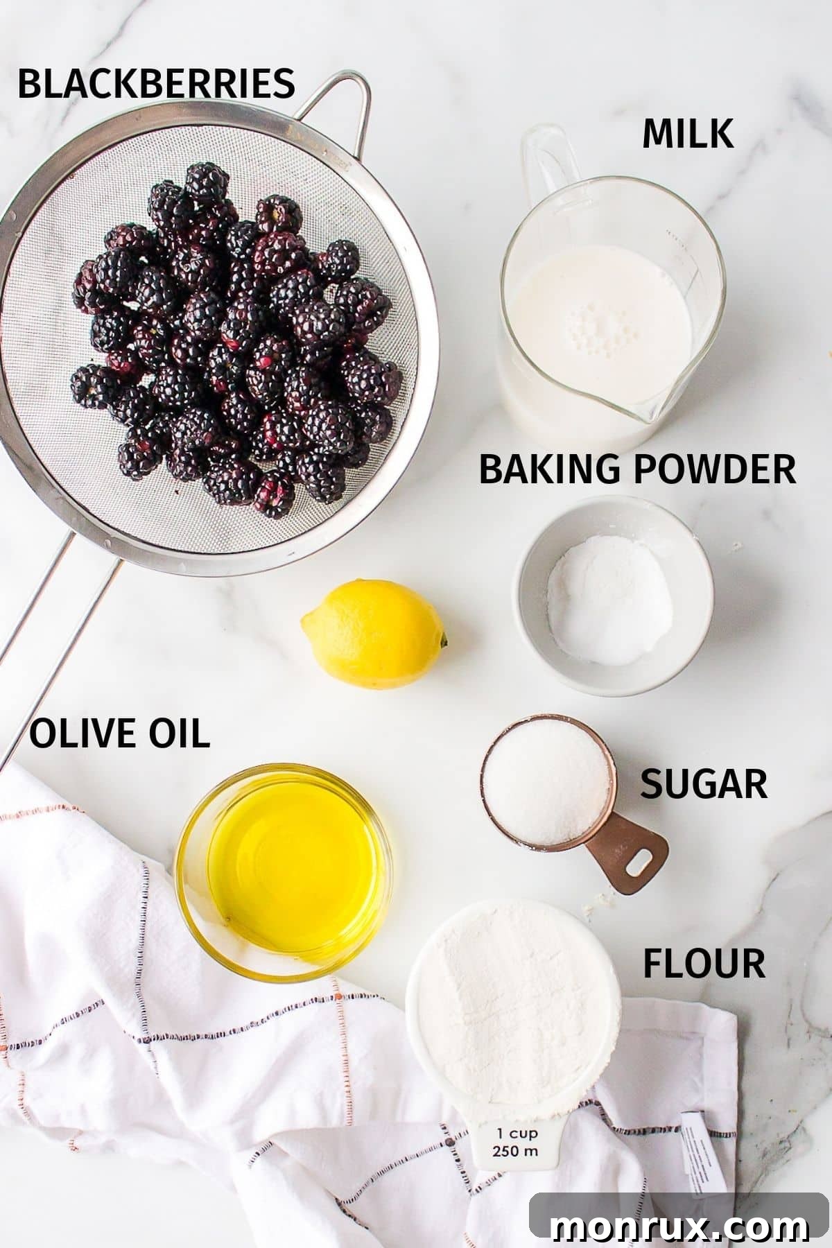 Ingredients for vegan blackberry muffins in small bowls on a white surface.