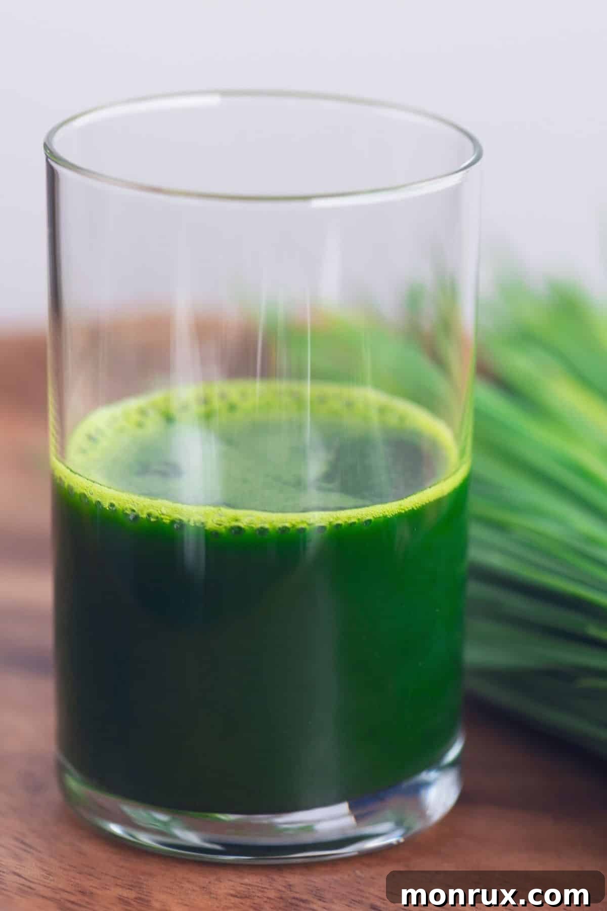 A small glass of vibrant green wheatgrass juice rests on a rustic wooden surface, highlighting its freshness and natural appeal.