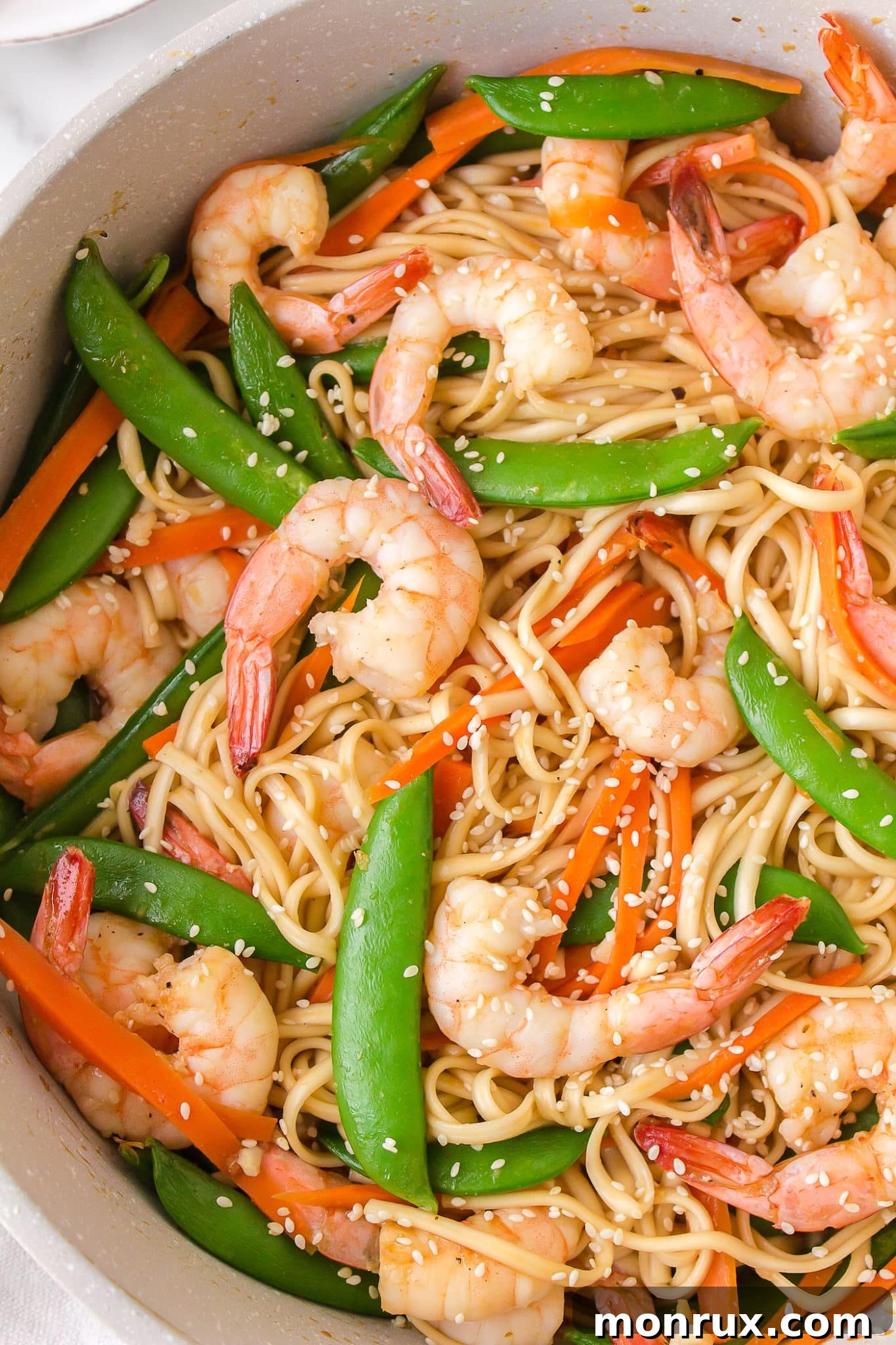 A vibrant bowl of Japanese Shrimp Udon stir-fry, featuring plump shrimp, green peas, and red bell peppers, garnished with sesame seeds.