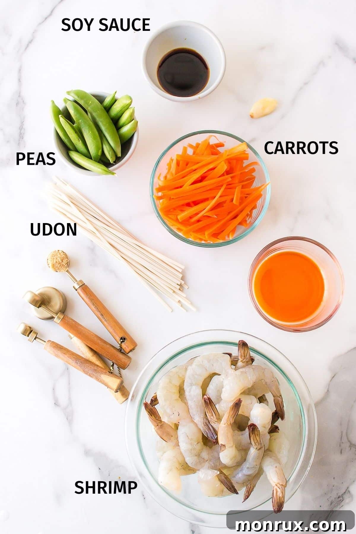 Various ingredients for shrimp udon, including fresh shrimp, carrots, sugar snap peas, garlic, and sauce components, neatly arranged in small bowls.