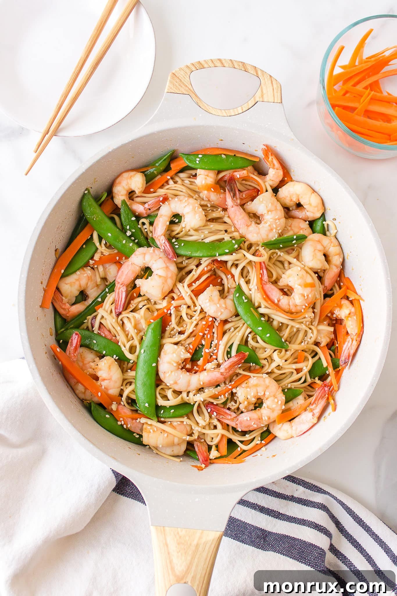 A close-up of a serving of Shrimp Udon with various vegetables, presented in a white bowl with chopsticks ready for eating.
