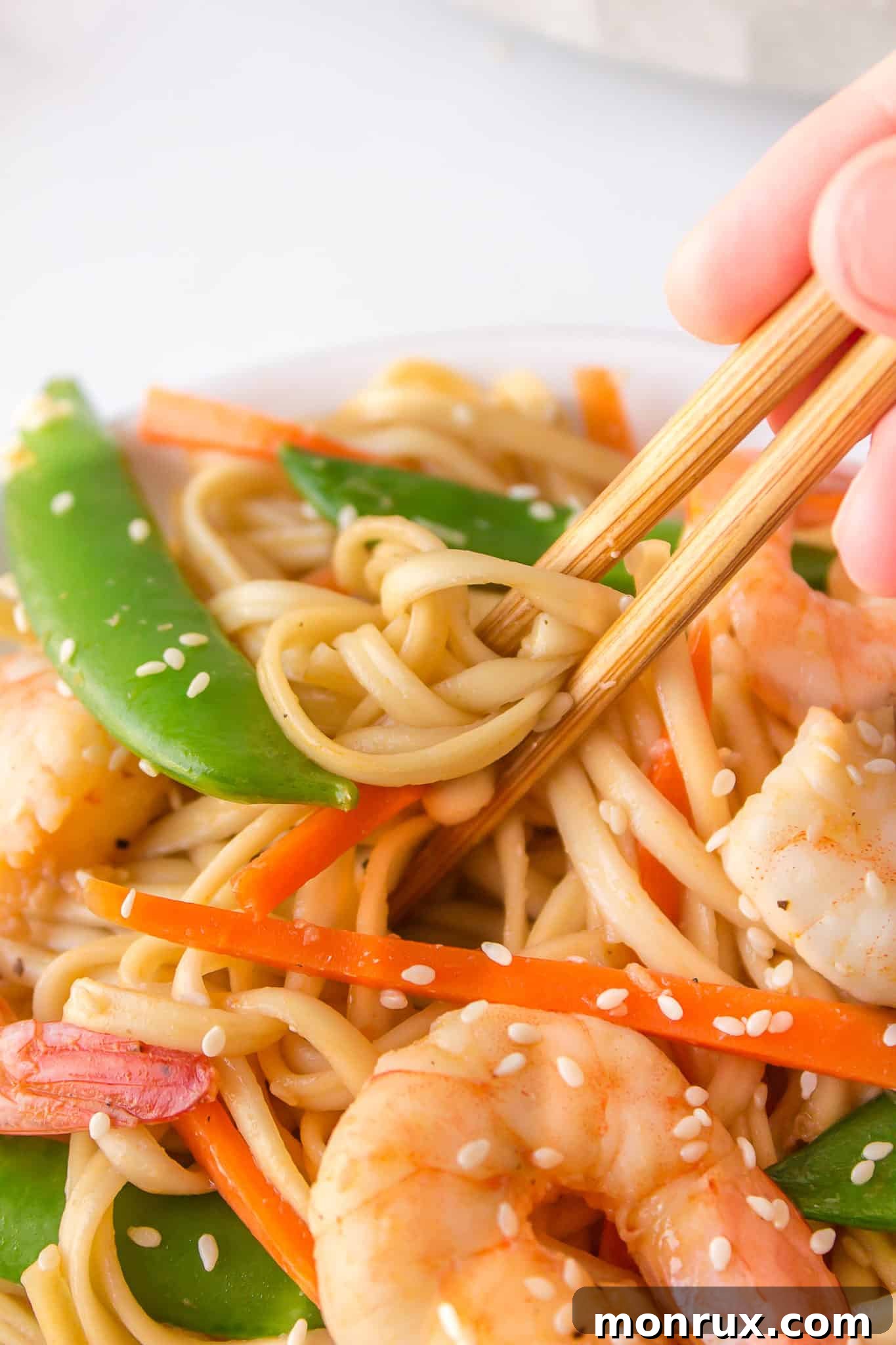 Chopsticks expertly lifting a tangle of saucy shrimp udon noodles, showcasing the coated ingredients and inviting texture.