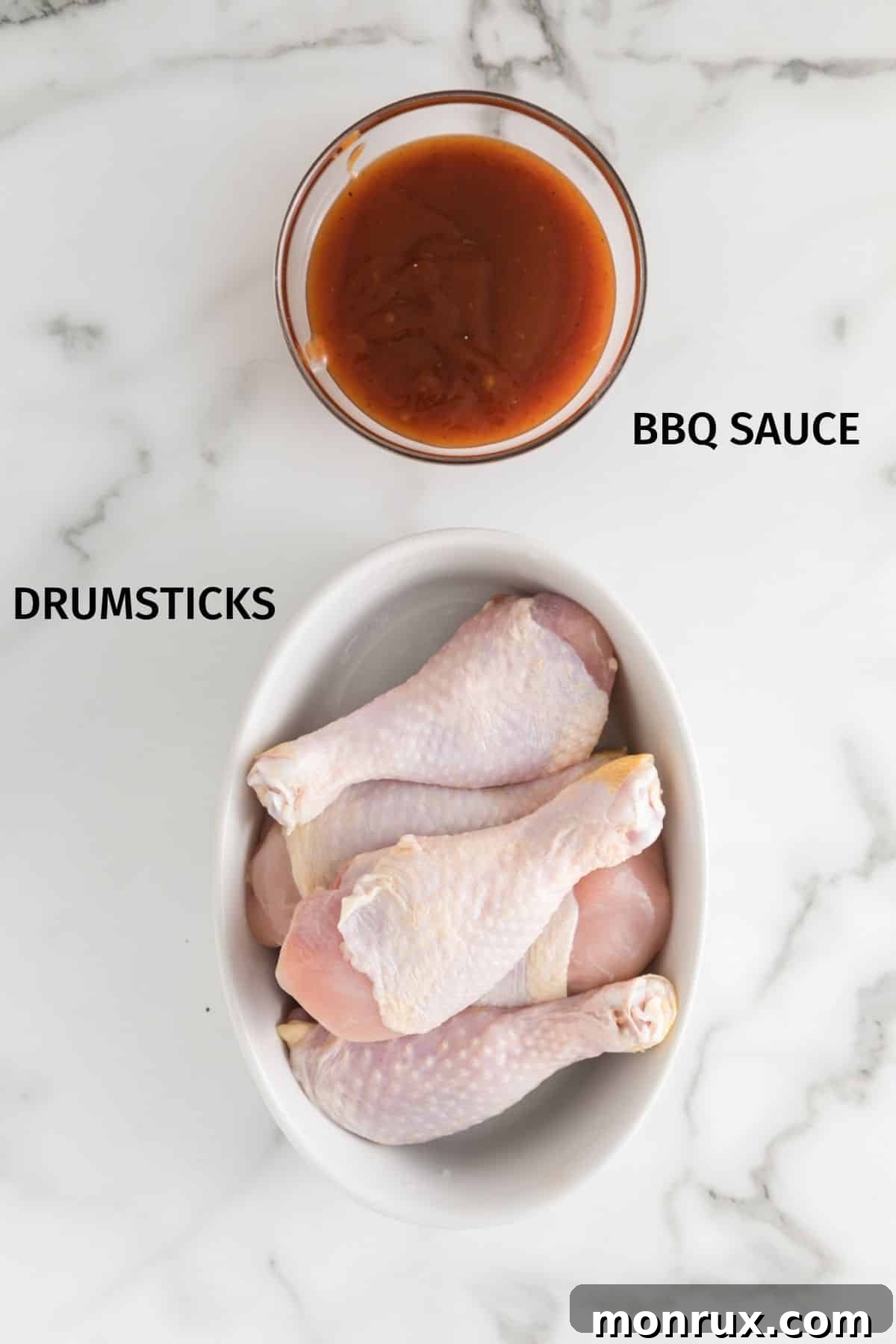 Chicken drumsticks and BBQ sauce in bowls on a white surface, ready for preparation.