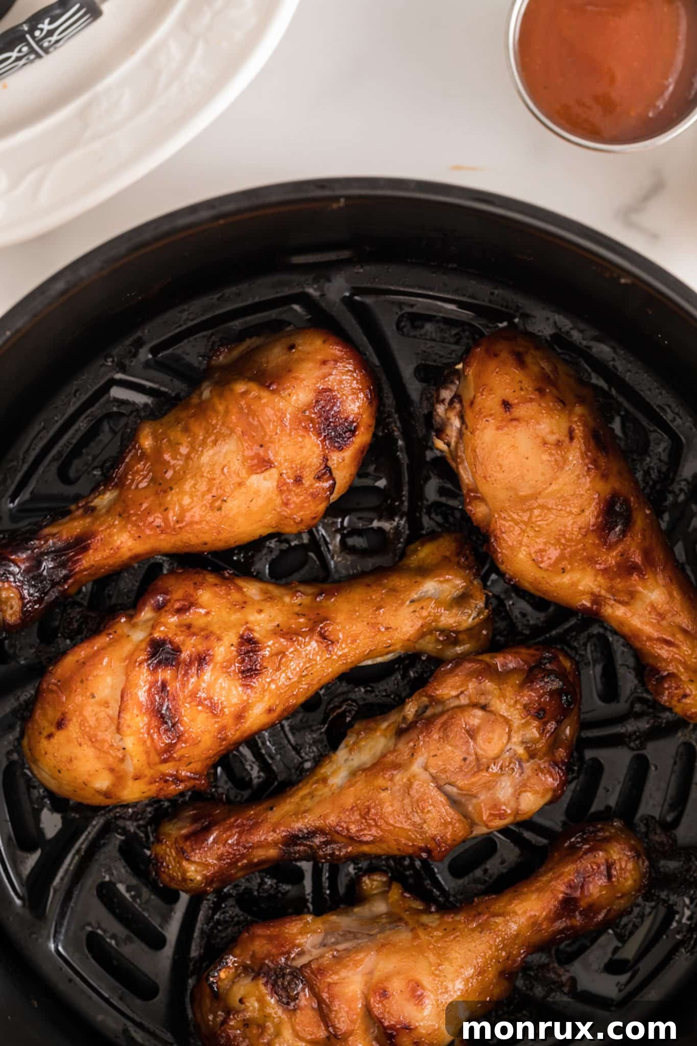 Cooked BBQ drumsticks glistening with sauce in the basket of an air fryer, ready to be served.