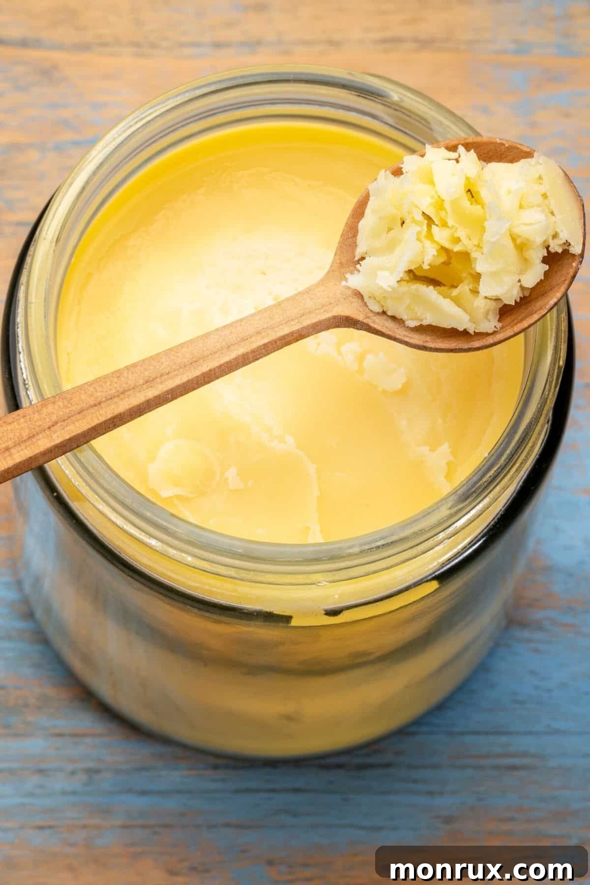 A wood spoon with a scoop of ghee over a full jar.