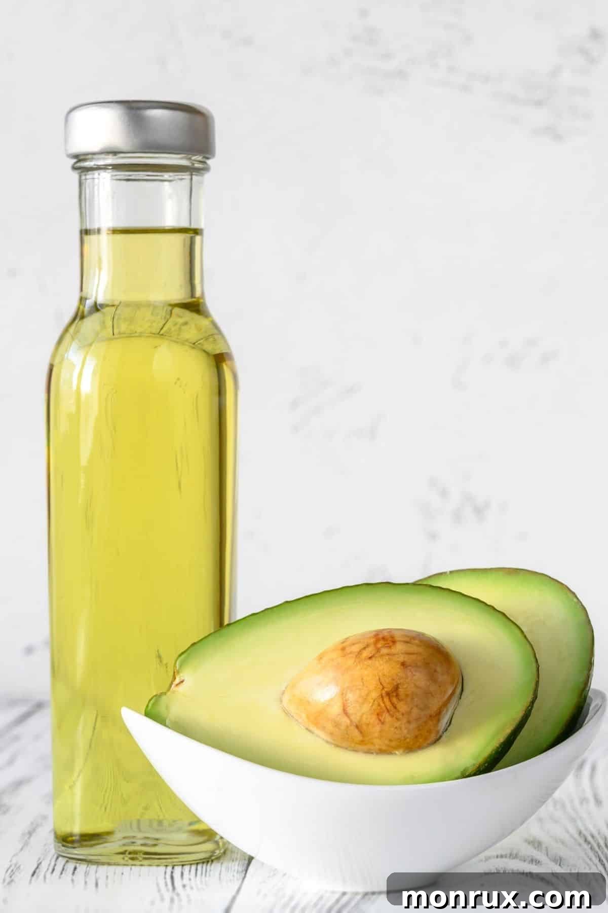 Jar of avocado oil next to a halved avocado.
