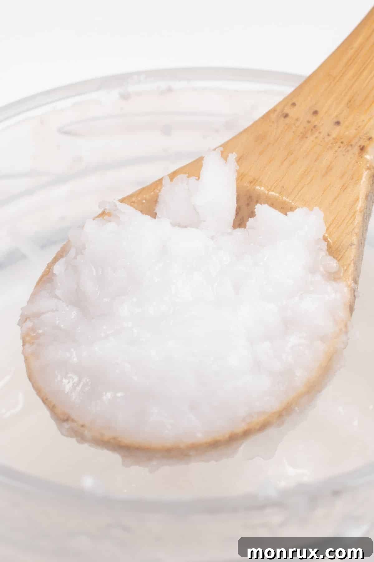 Coconut oil in a wooden spoon over a jar.