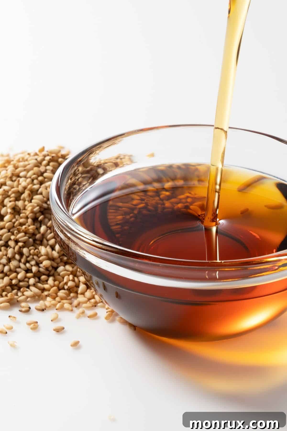 Small bowl of sesame oil next to sesame seeds on a counter.