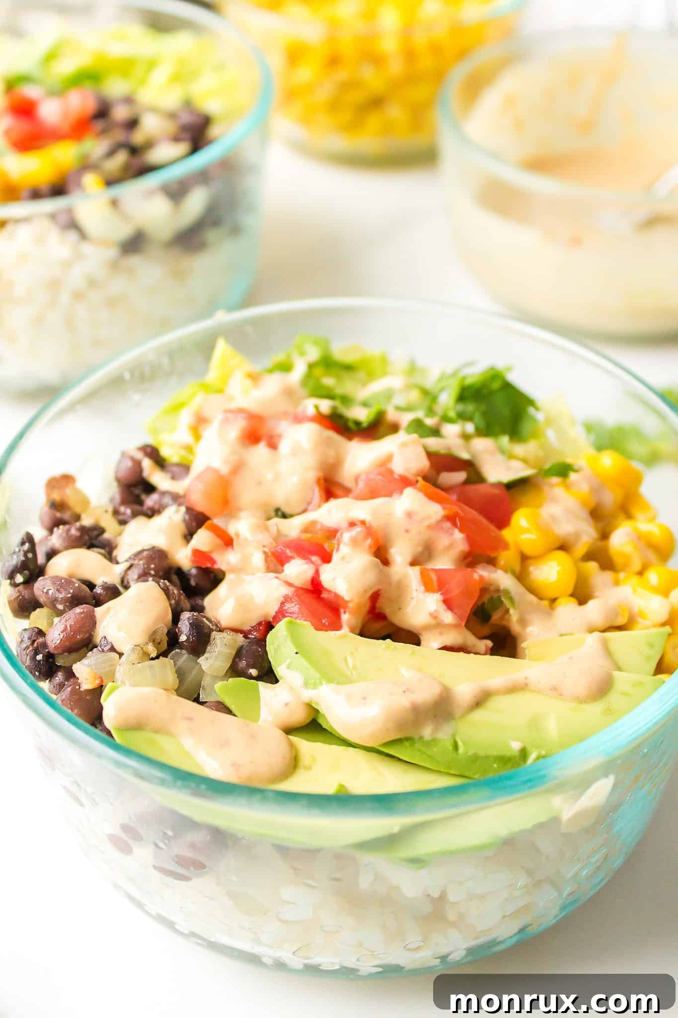 A clear glass bowl filled with a healthy and colorful Mexican Buddha Bowl, featuring brown rice, black beans, corn, avocado, and fresh cilantro, drizzled with a creamy tahini sauce.
