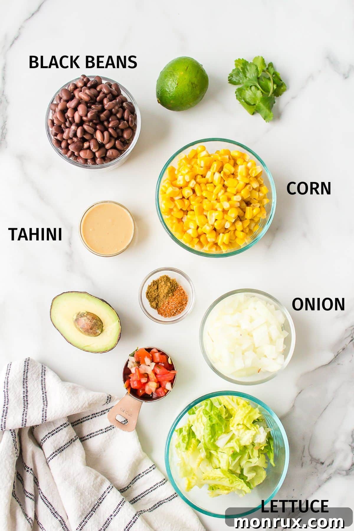 Individual bowls containing fresh ingredients for Mexican Buddha Bowls, including black beans, corn, chopped avocado, cilantro, and limes, arranged on a white background.