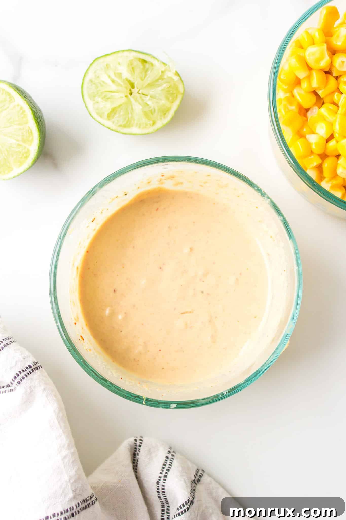 A small glass bowl filled with creamy spicy tahini sauce, placed beside a bowl of bright yellow corn kernels.