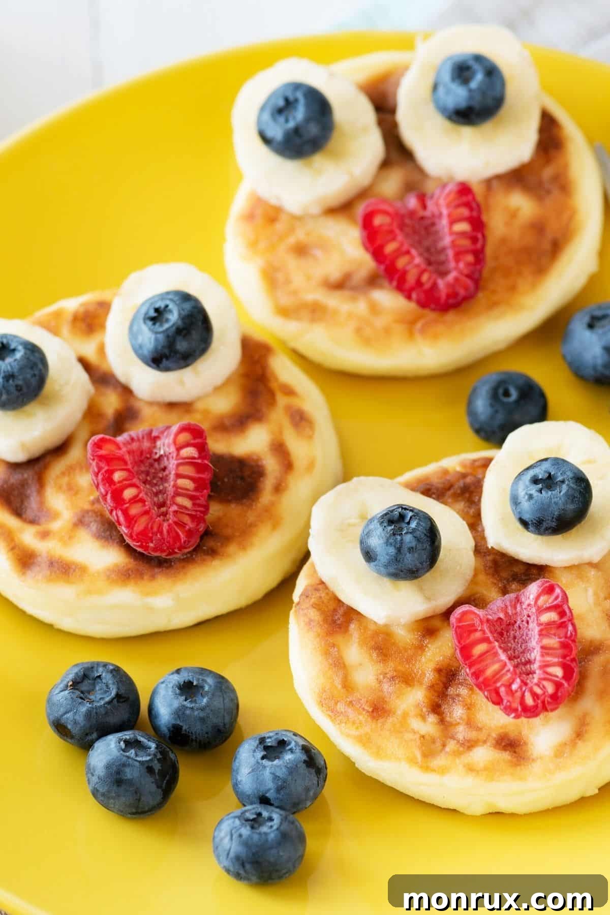 Pancakes with fruit faces on a yellow plate.