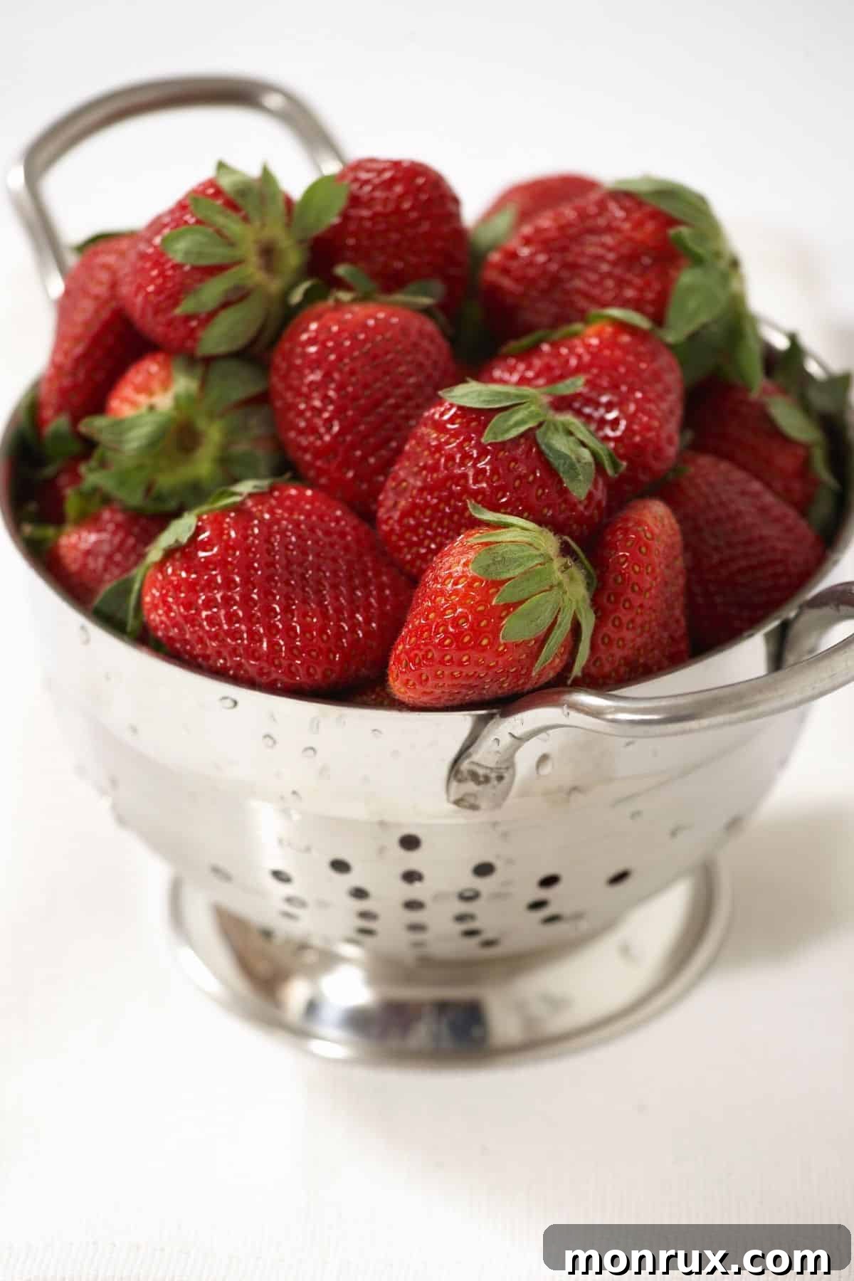 Fresh, ripe strawberries are rinsed in a colander, ready for juicing.