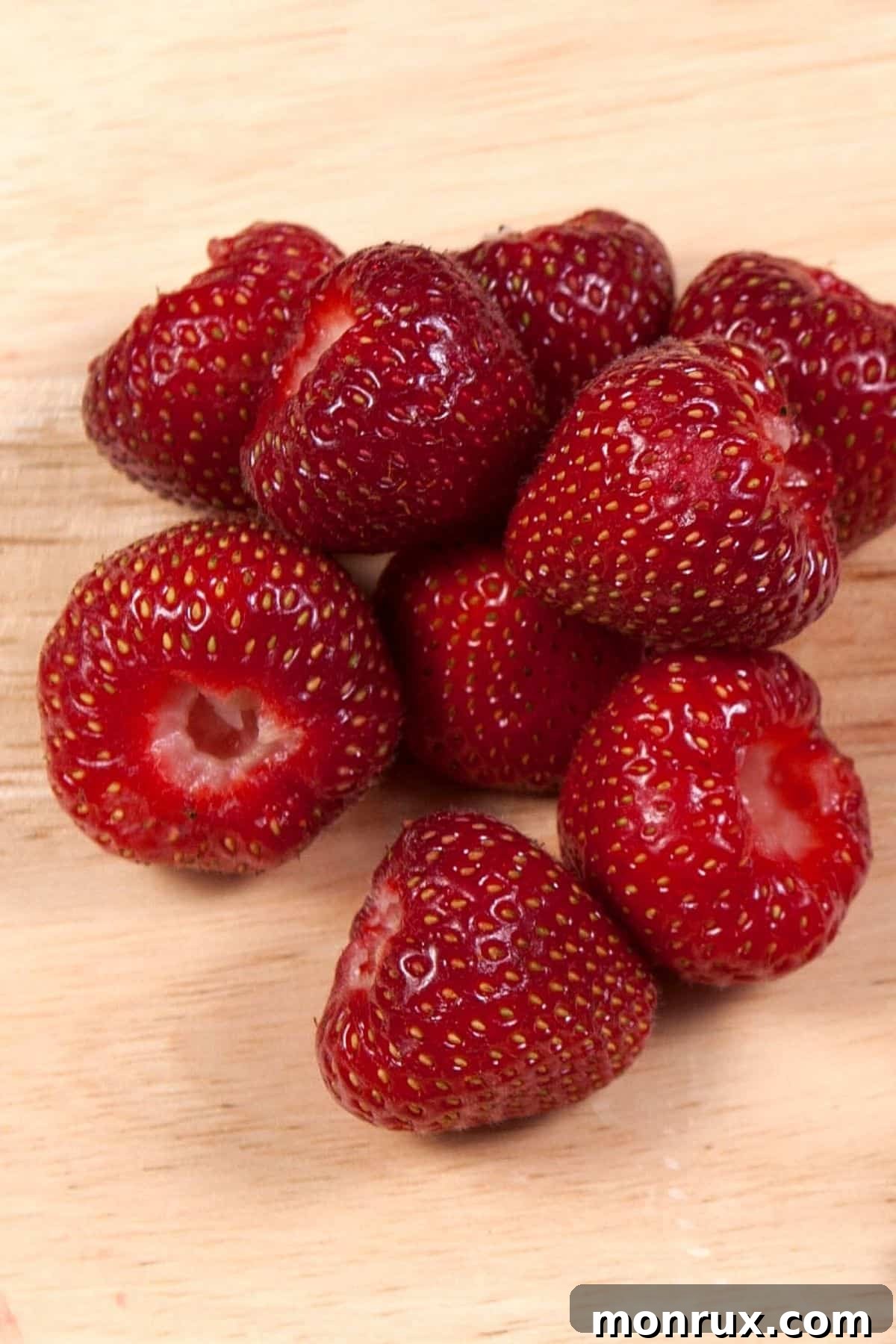 Fresh strawberries, with their green hulls removed, are neatly arranged on a white cutting board, ready for the next step in juicing.