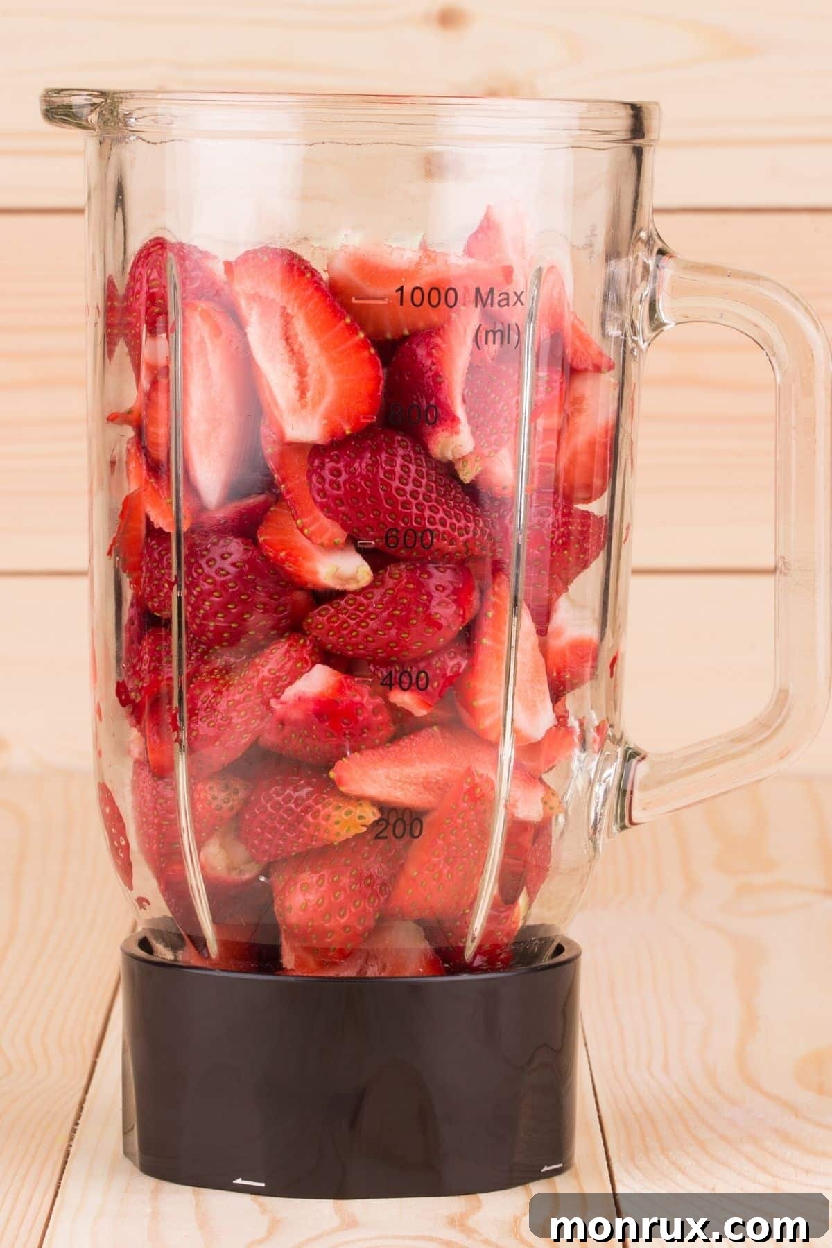 Quartered strawberries, along with a bit of water, are shown in a blender jar, prepared for blending into juice.
