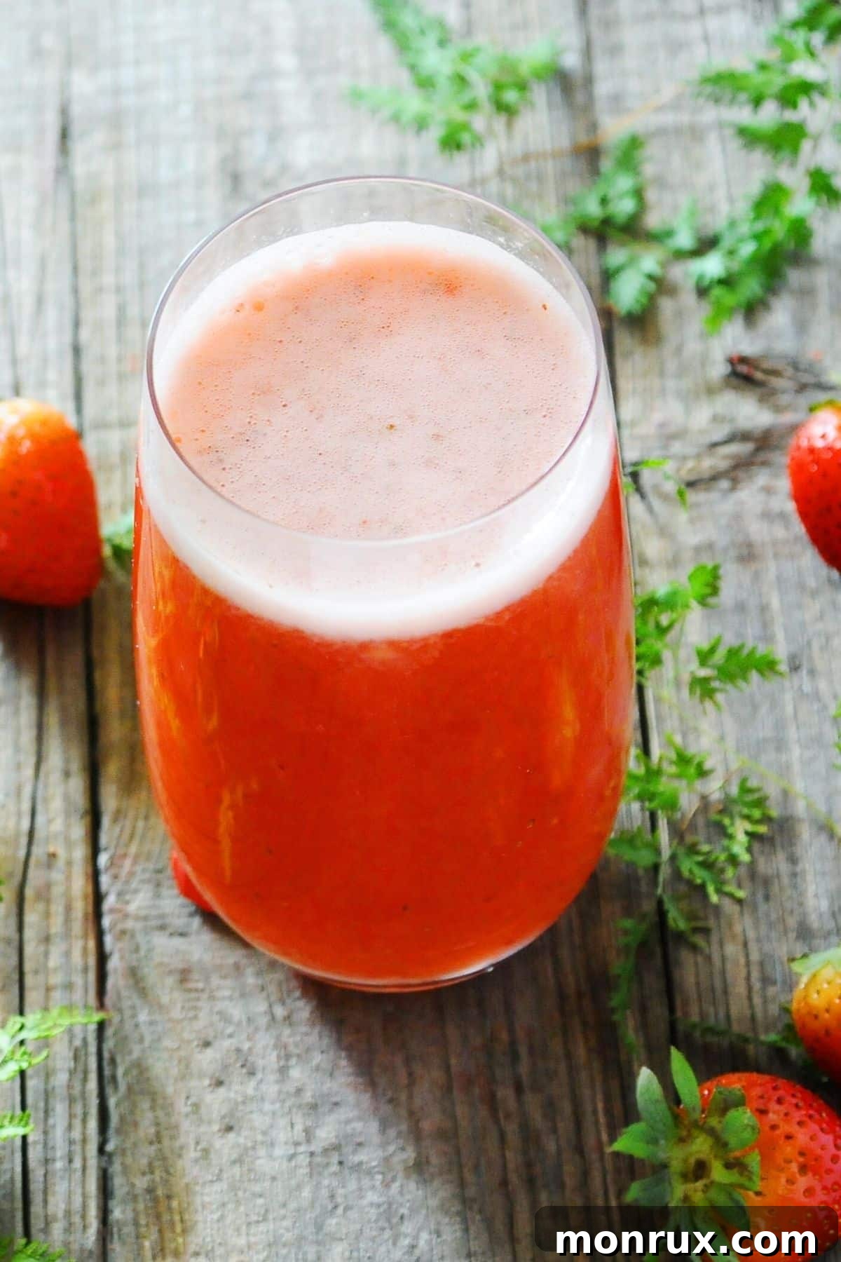 A tall glass of frothy, red strawberry juice is presented on a clean surface, highlighting its vibrant color and fresh appeal.