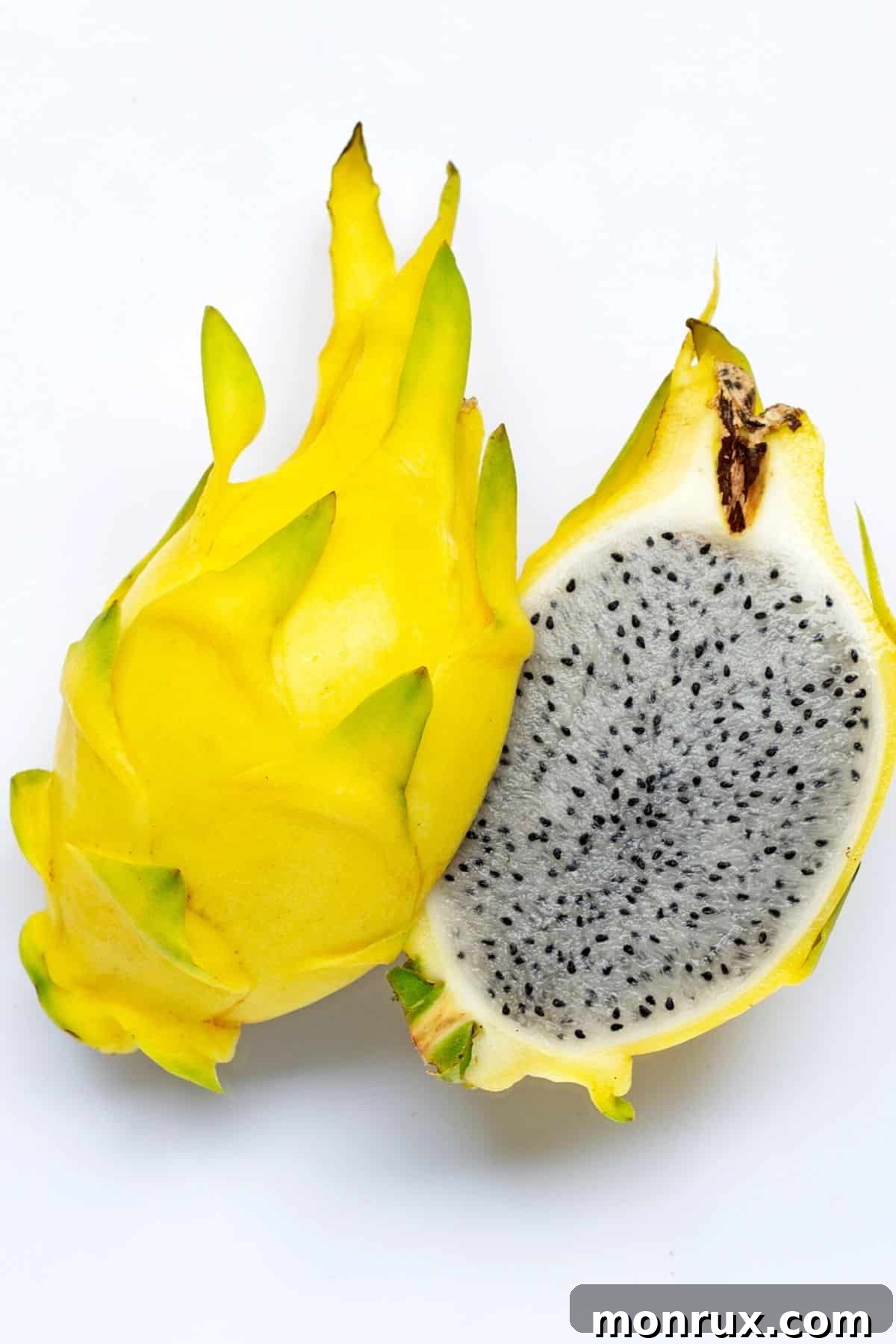A large, vibrant yellow dragon fruit, freshly cut in half to reveal its inviting white flesh dotted with tiny black seeds, artfully arranged on a clean white surface.