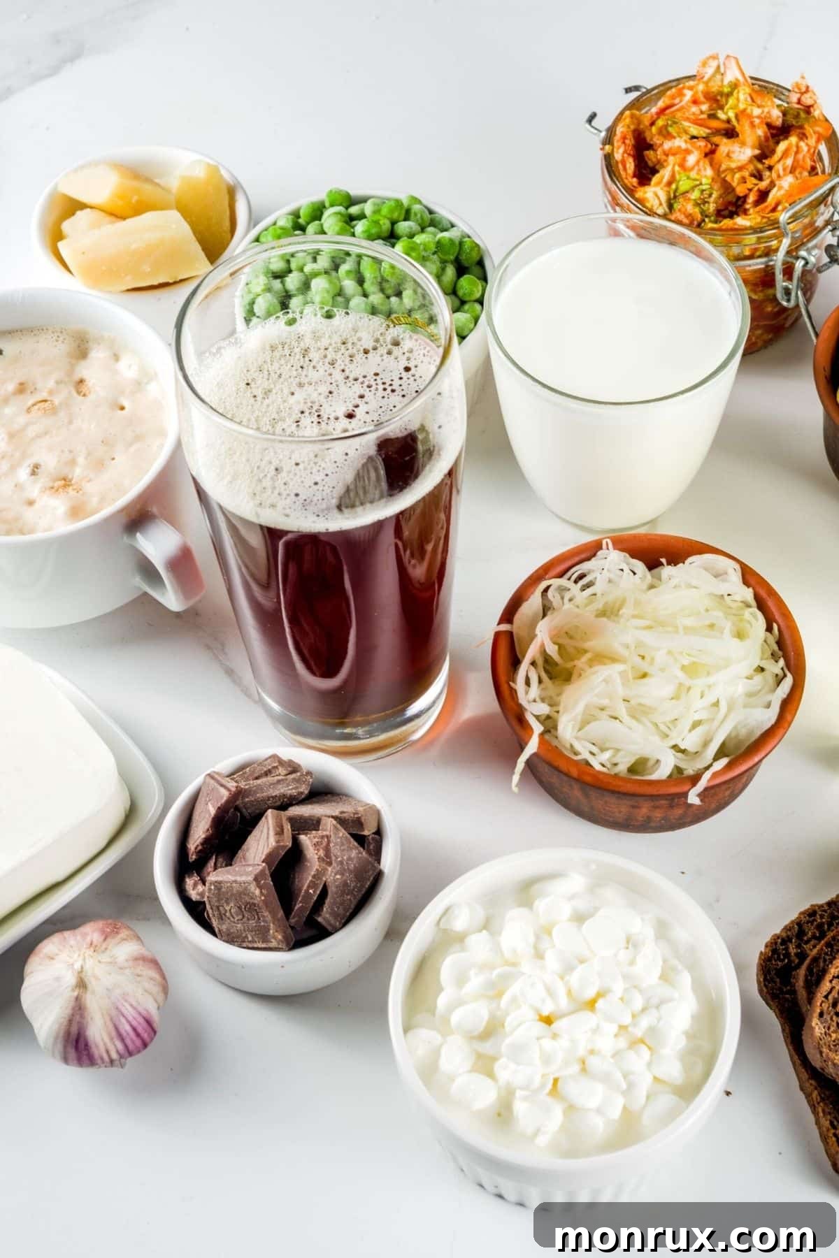 Various gut healing foods in glasses and bowls on a white surface, including bone broth, yogurt, greens, and fish.