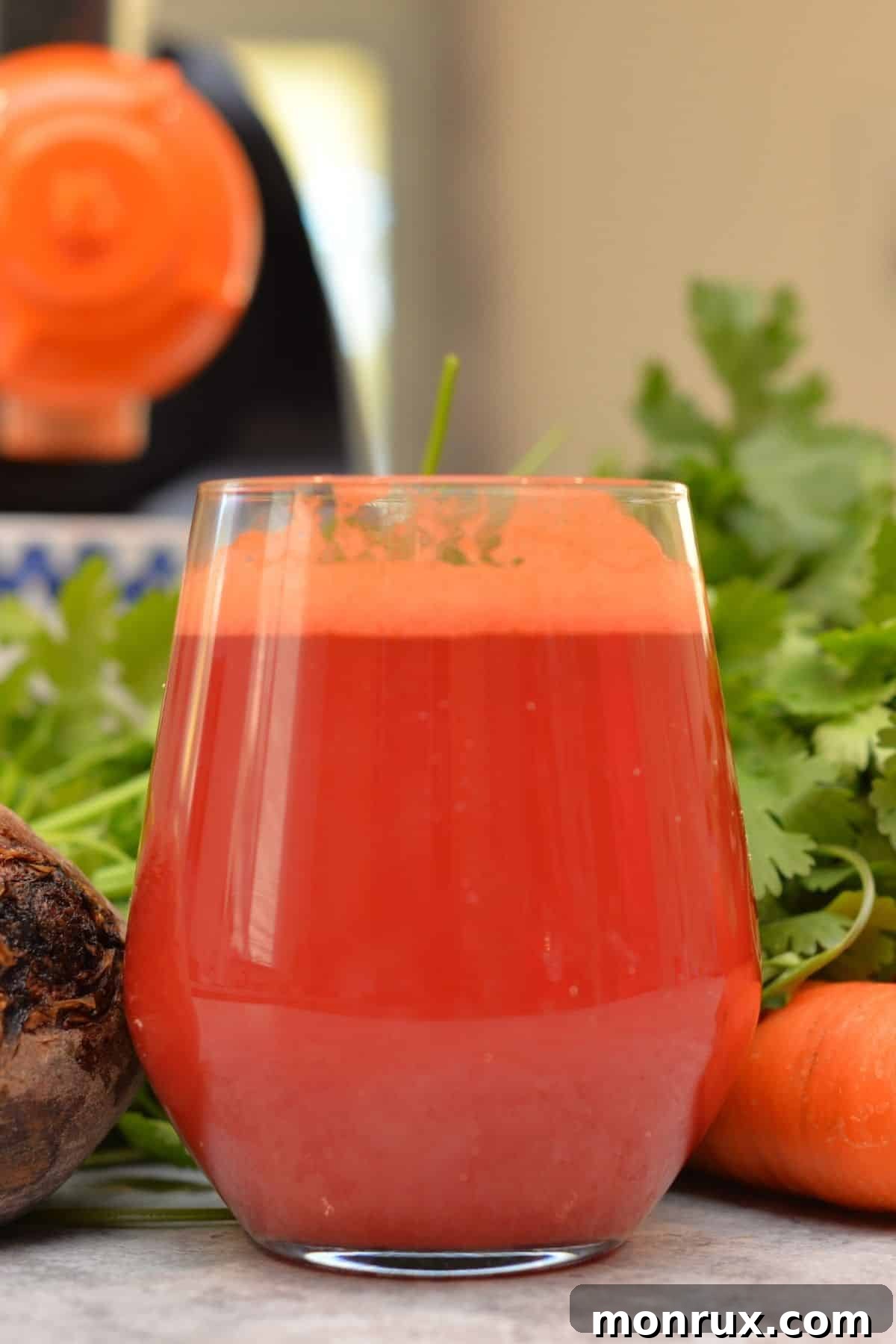 A refreshing glass of homemade beet carrot juice on a rustic wooden table, garnished with a carrot top.