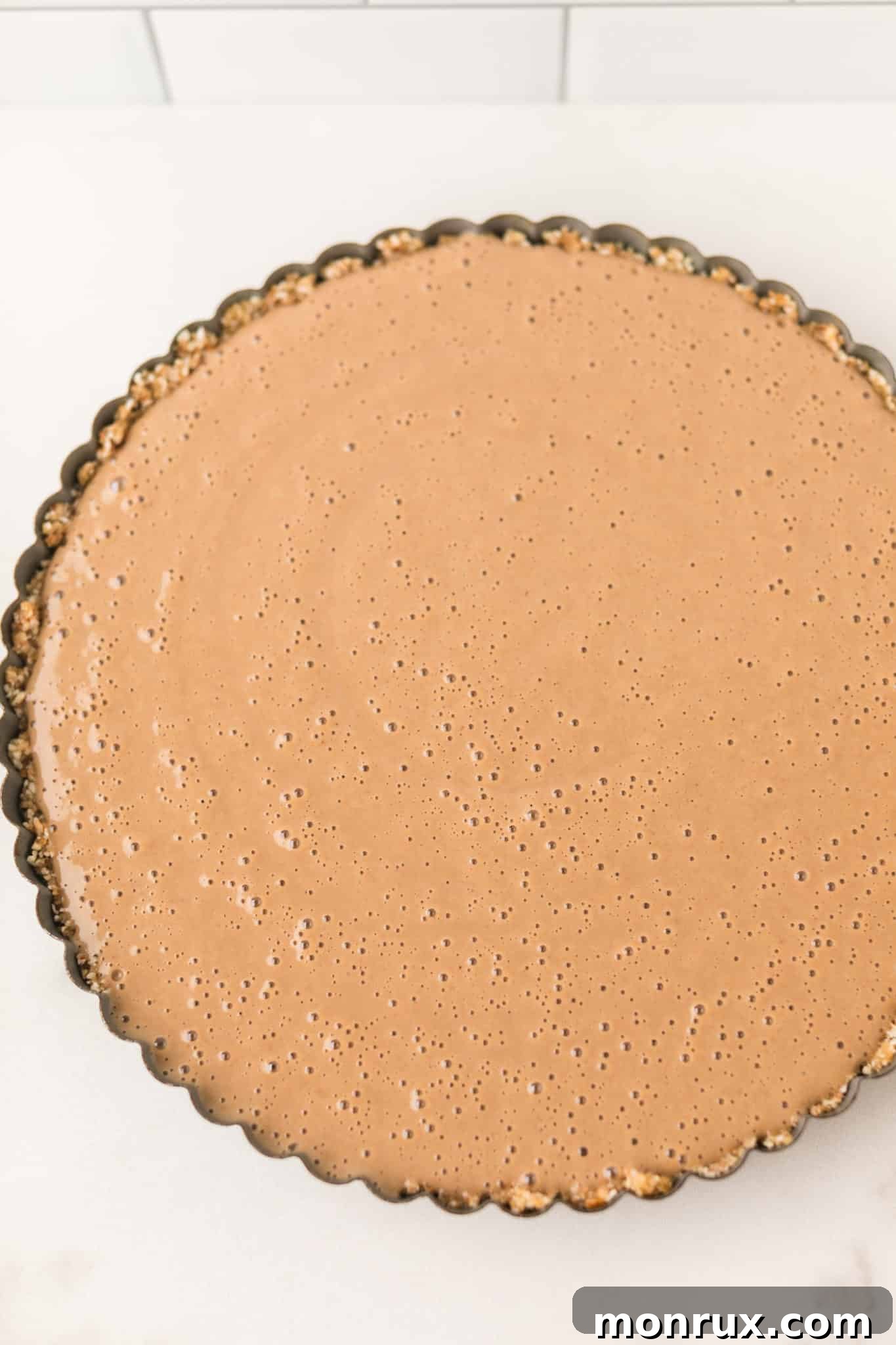 The vegan peanut butter tofu pie, freshly assembled in its crust, sits ready to be placed in the refrigerator for chilling, ensuring a firm and delightful dessert.