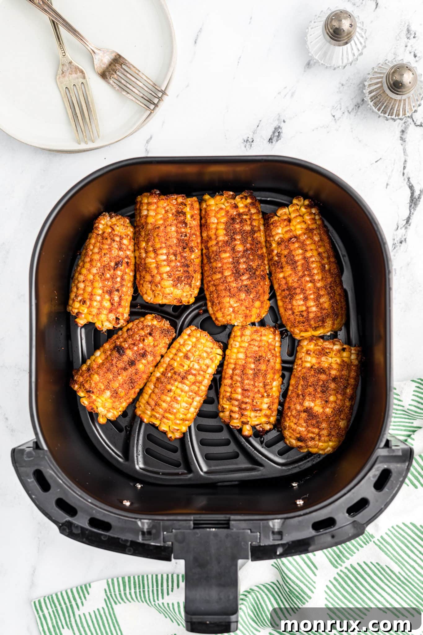 Seasoned corn ribs cooking and curling in the basket of an air fryer.