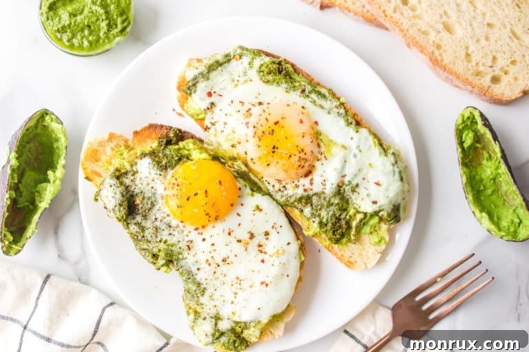 Pesto fried eggs on slices of avocado toast on a white plate.