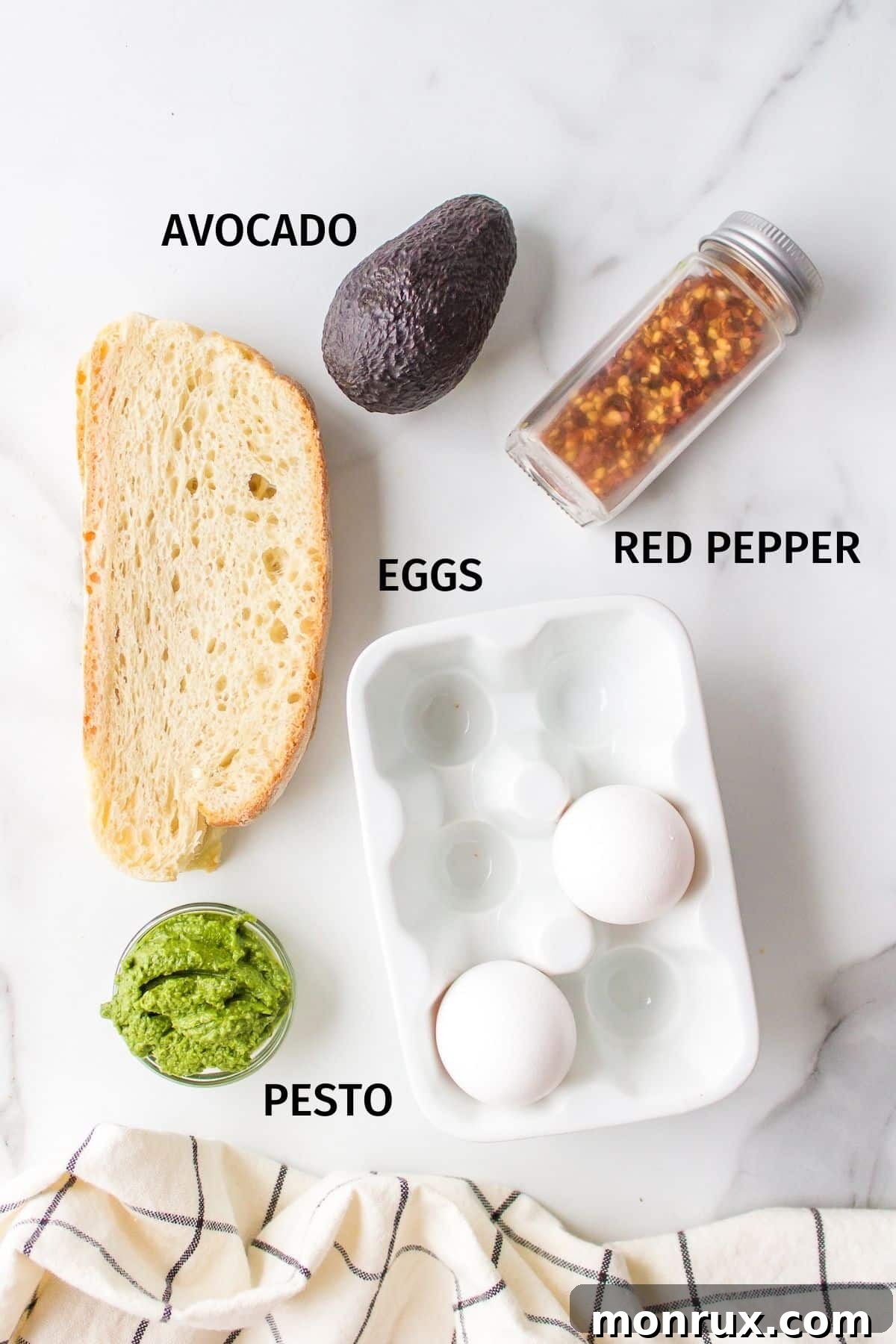 Ingredients for making pesto eggs on avocado toast laid out on a white background, including eggs, avocado, bread, and a jar of pesto.