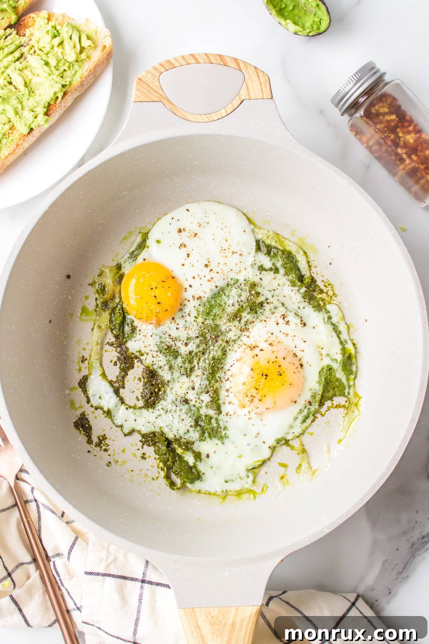 Two eggs frying gently in a skillet filled with bubbling green pesto sauce.