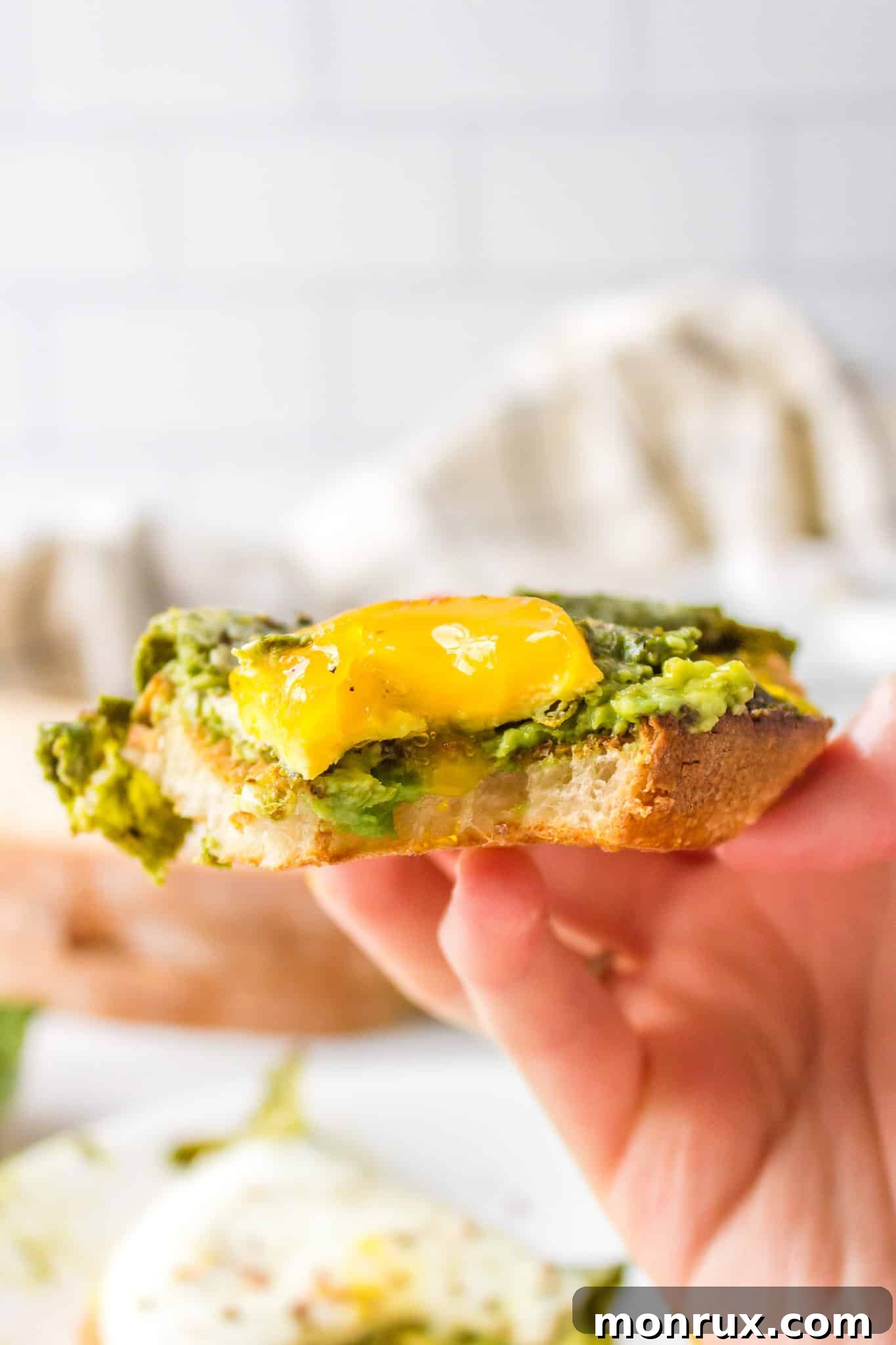 Side view of a bite taken from pesto eggs on avocado toast, showcasing the runny yolk and creamy avocado.