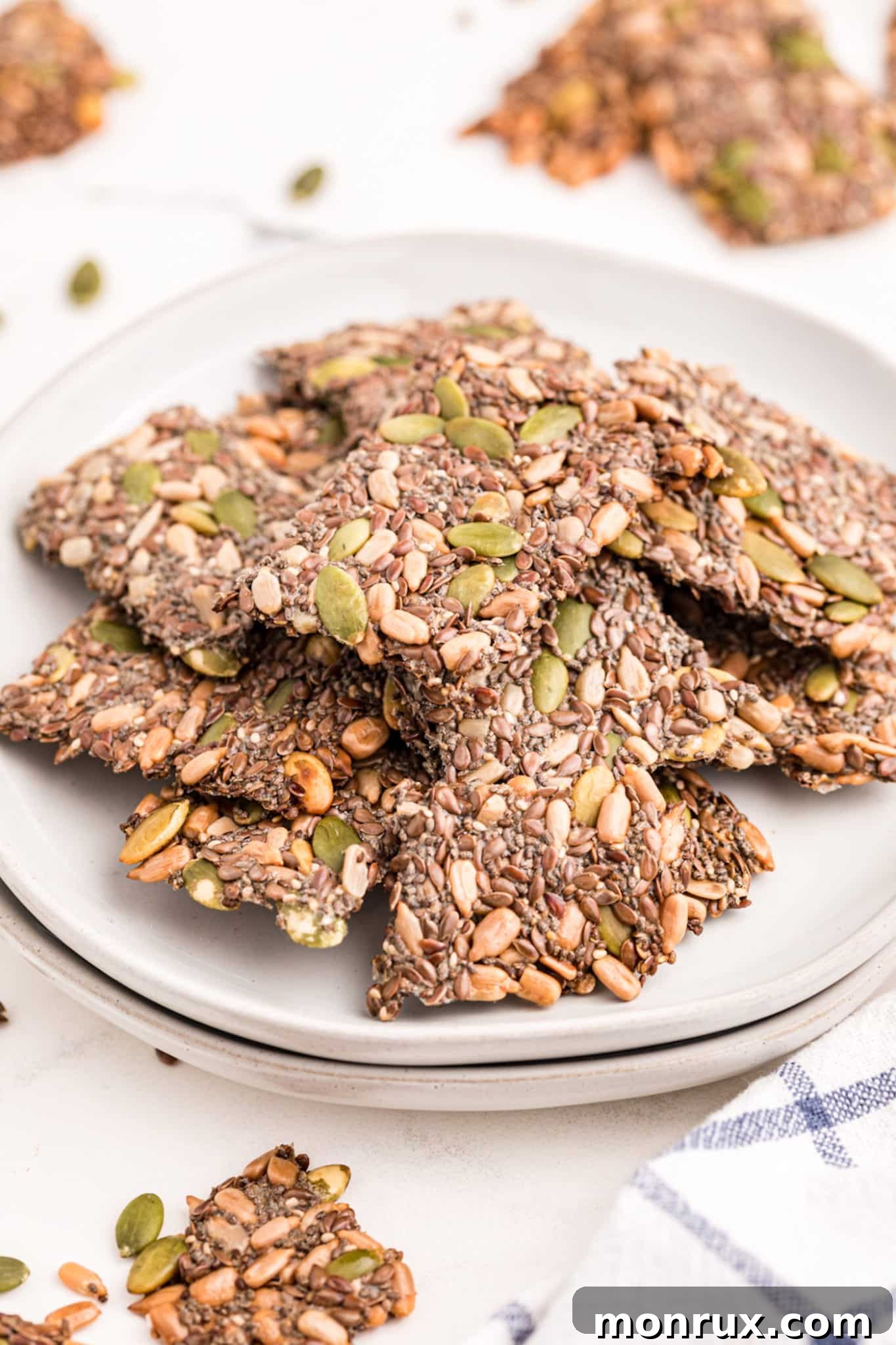Homemade seed crackers piled high on a pristine white plate, showcasing their rustic texture and golden hue.