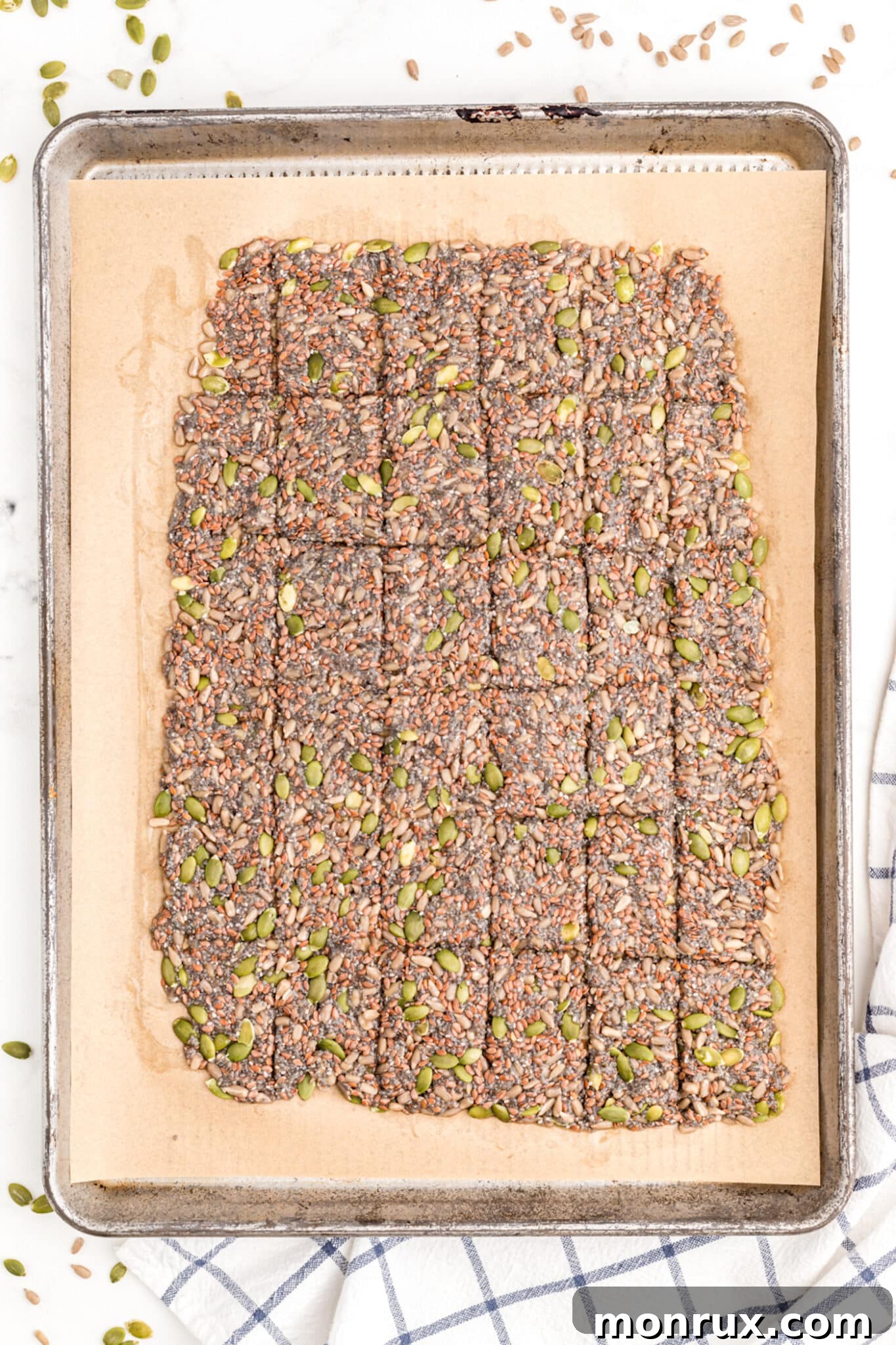 Scored seed cracker dough on a baking sheet, golden brown and ready to be baked in the oven until perfectly crisp.
