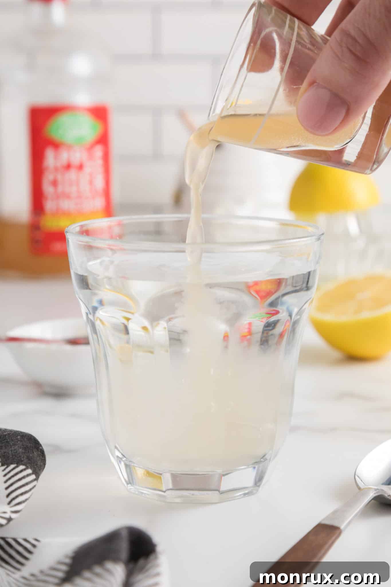 Pouring a shot of apple cider vinegar into a glass of water, illustrating the first step of the recipe.