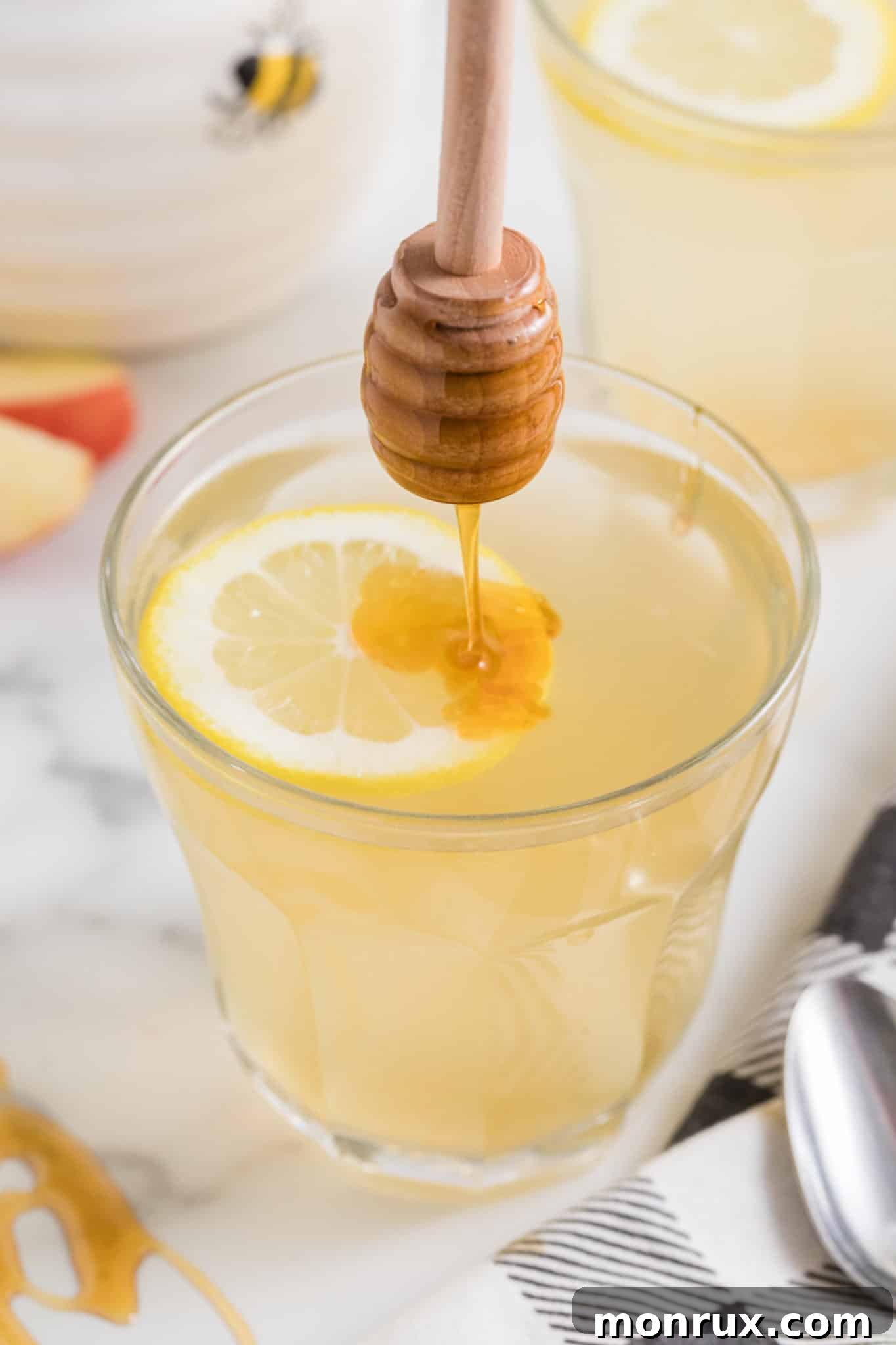 Drizzling honey into a glass of lemon ACV drink, adding a touch of sweetness.