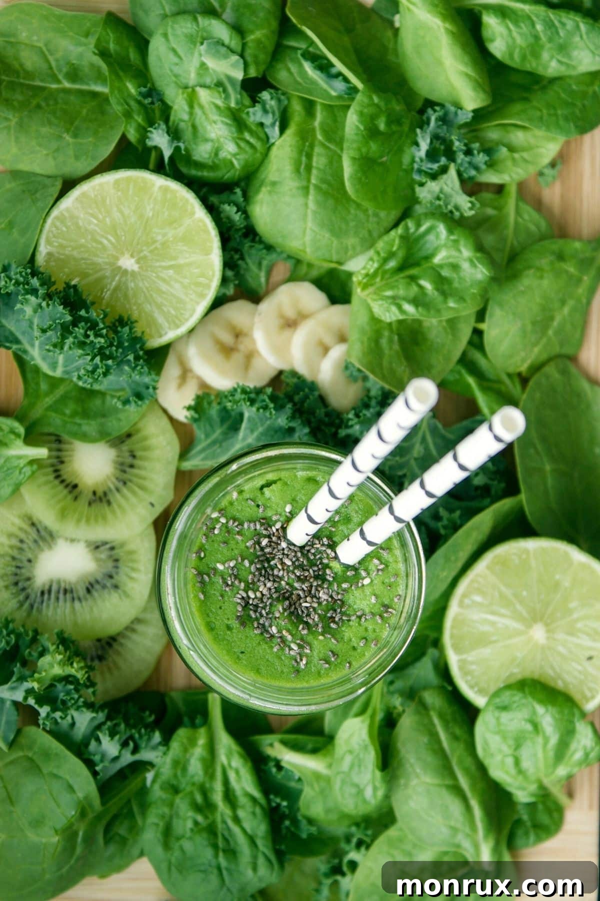 A vibrant green smoothie in a glass with a straw, surrounded by fresh green fruits and vegetables on a rustic wooden board.
