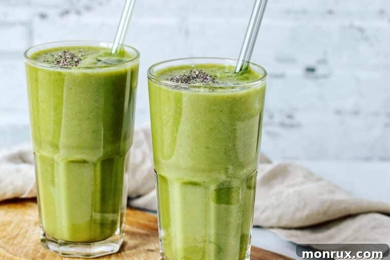 A basic green smoothie in a glass with chia seeds, a metal straw, and a fresh kiwi slice, set on a rustic table.