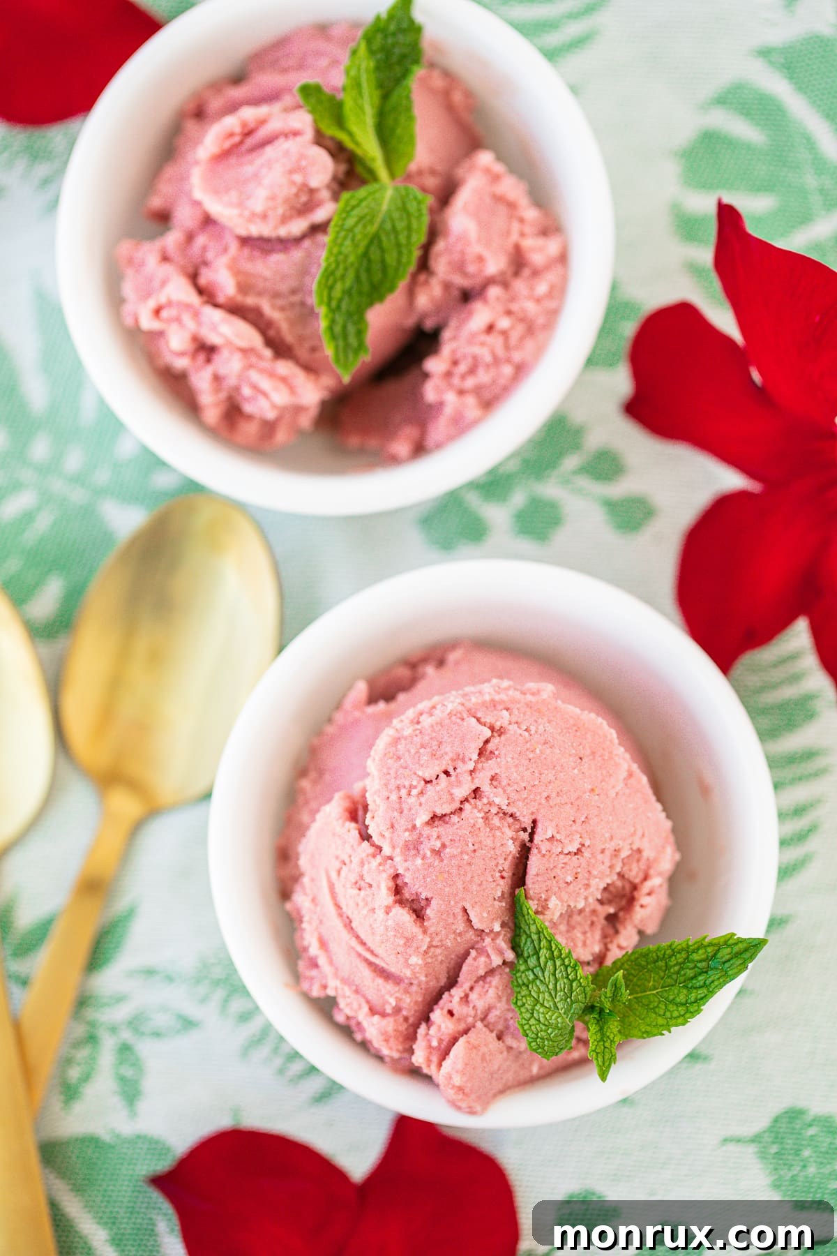 Two bowls of vibrant pink vegan strawberry ice cream garnished with fresh mint.