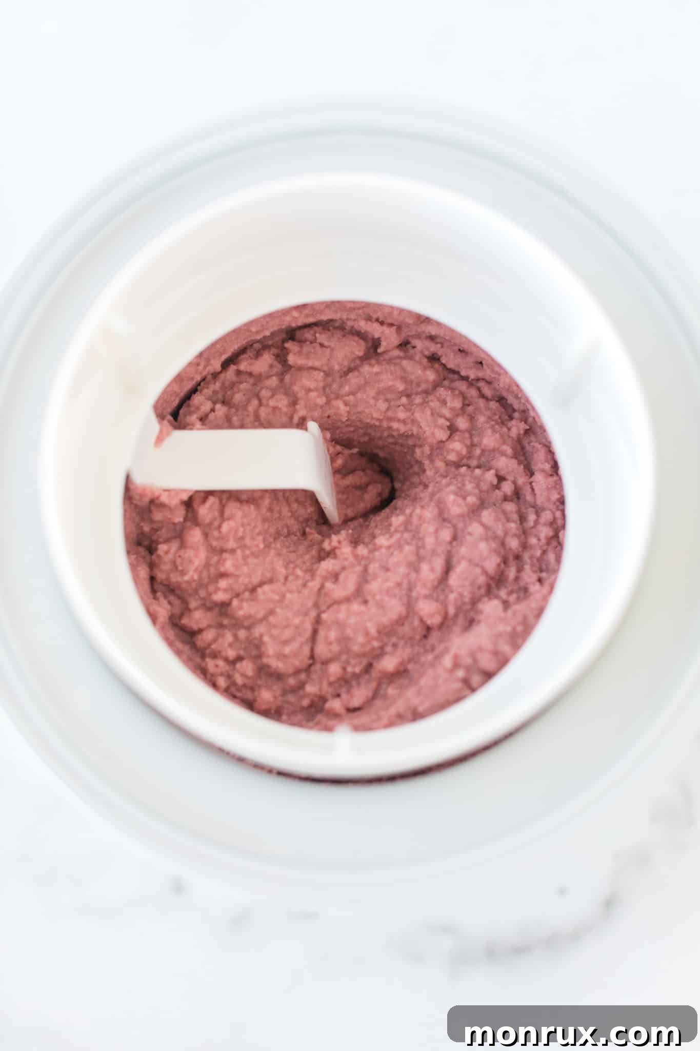 Churned strawberry ice cream inside an ice cream maker, showing a soft, creamy texture.