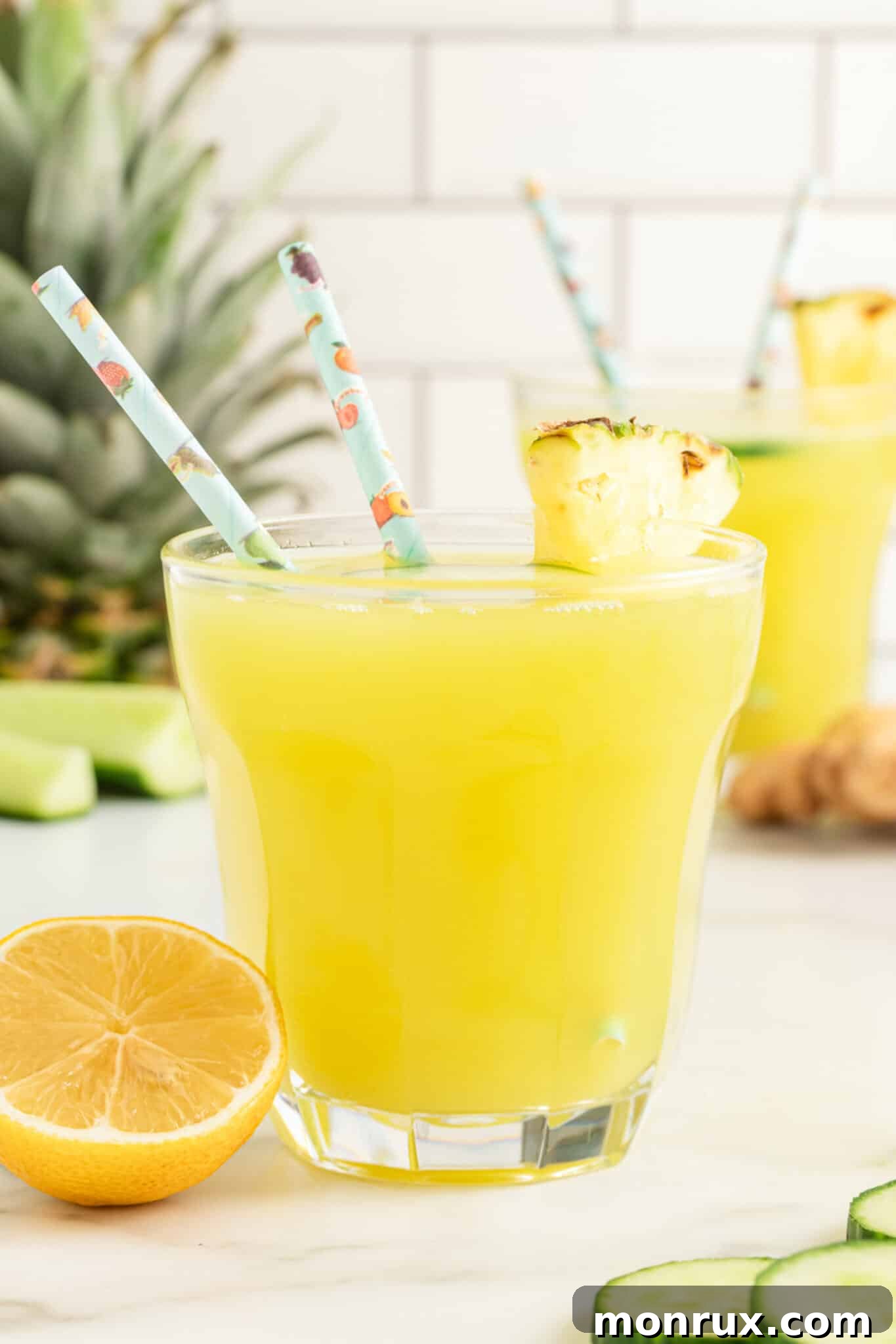 Closeup of a glass of pineapple cucumber juice with two straws.