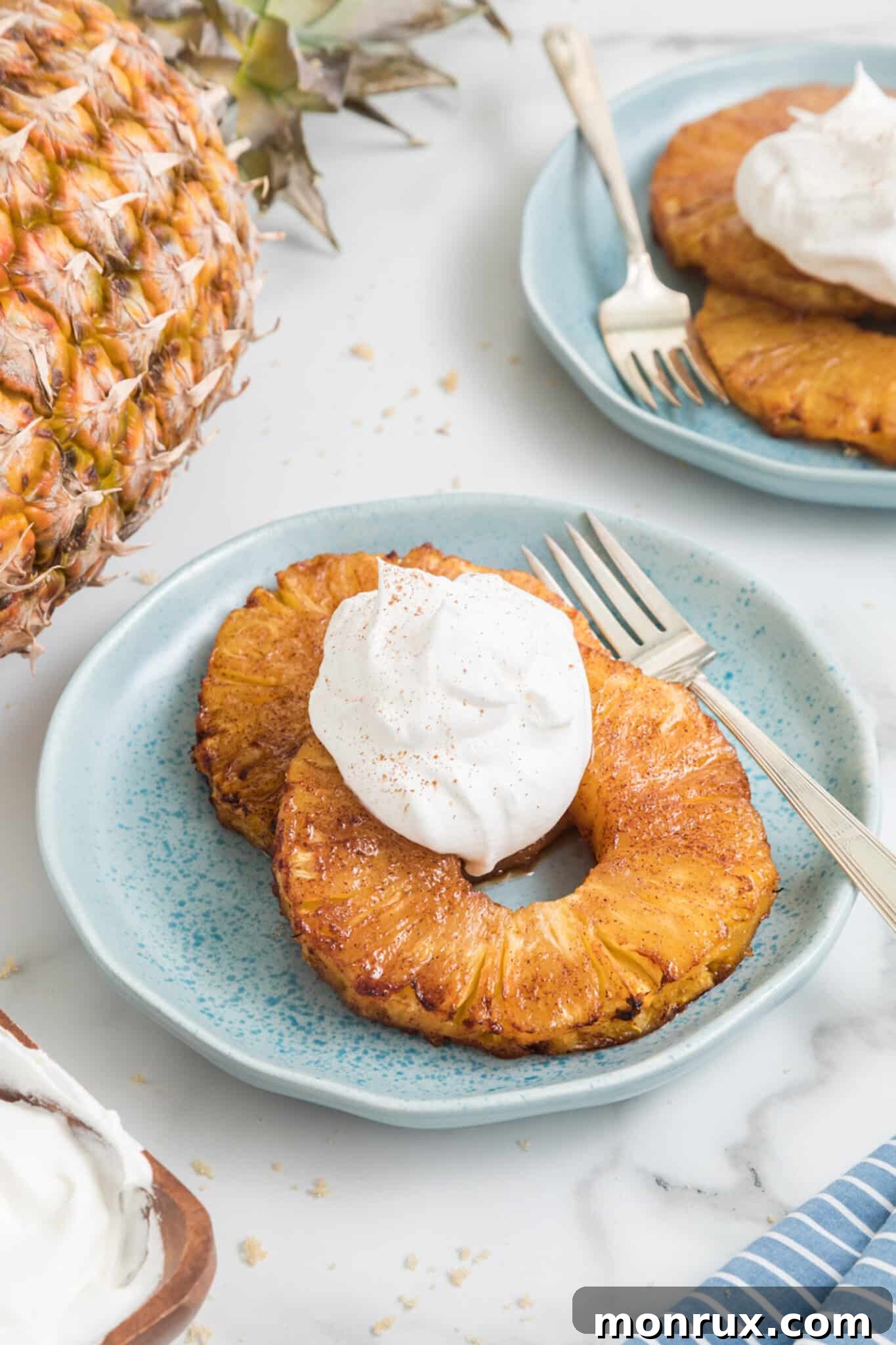 Two air fried pineapple rings topped with whipped cream on a small blue plate.