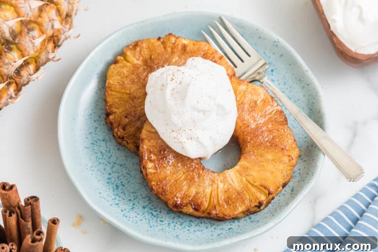 Two air fried pineapple rings topped with whipped cream on a small blue plate.