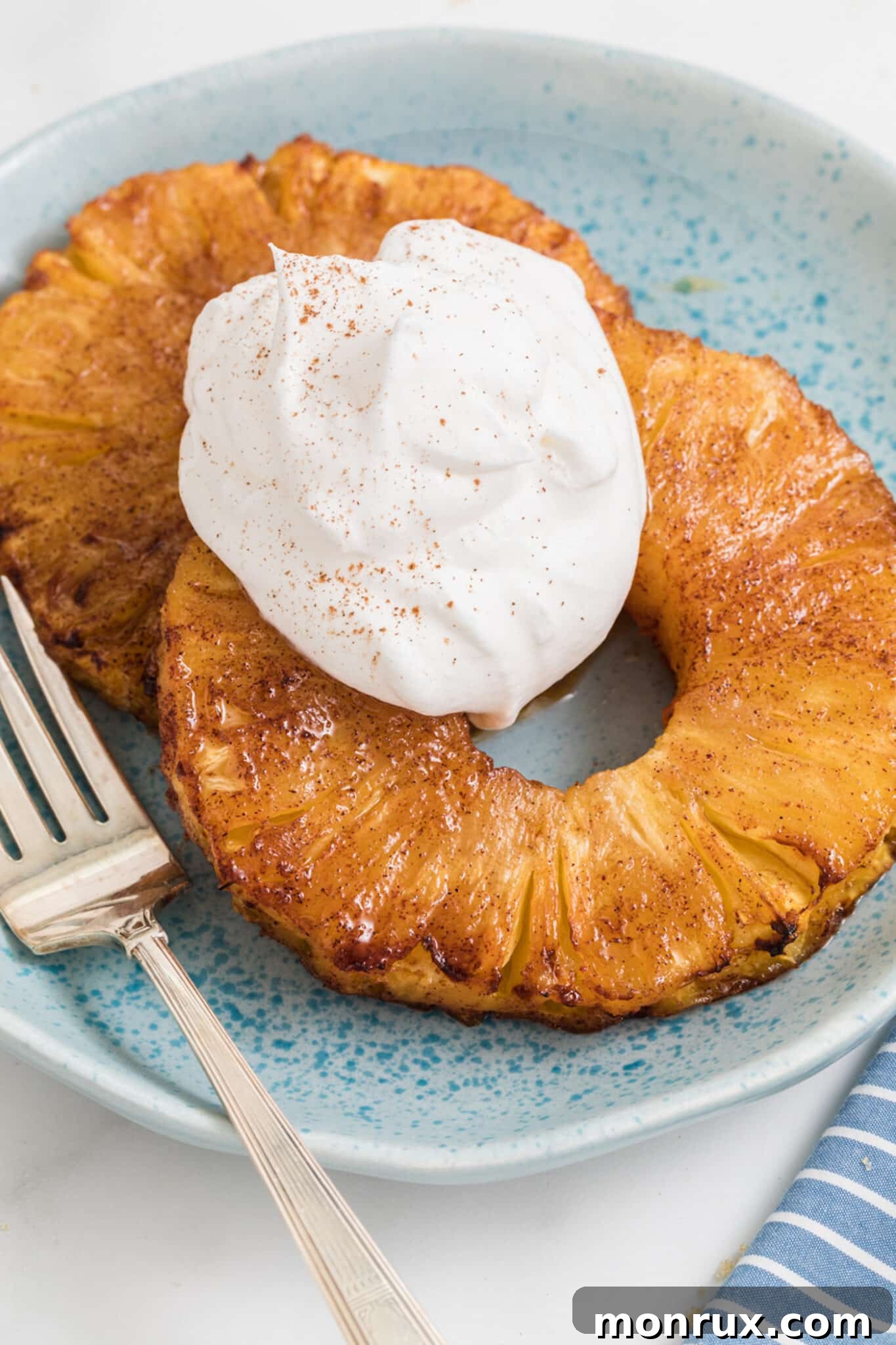 air fryer grill pineapple on plate with whipped cream and fork.