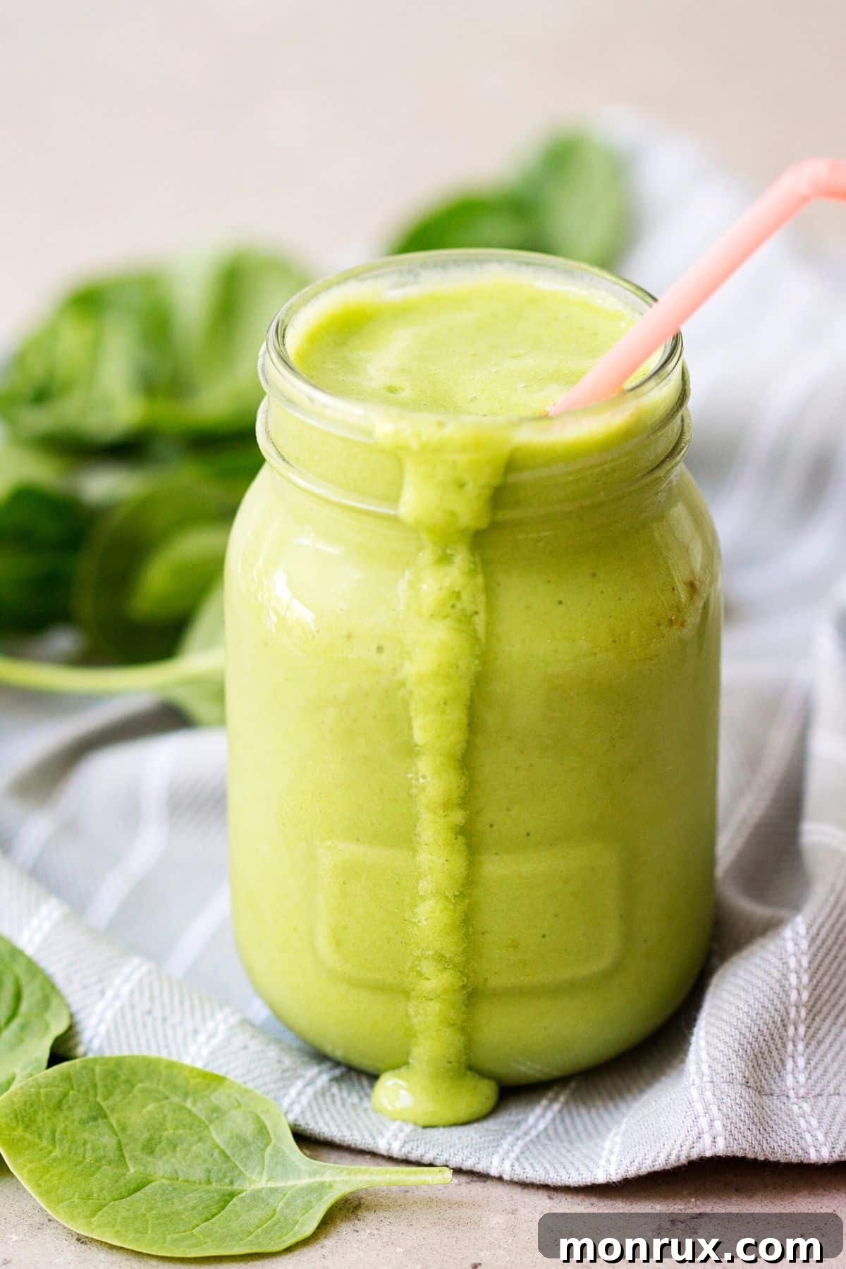Vibrant green spinach and fruit smoothie in a glass with a straw, ready to be enjoyed.