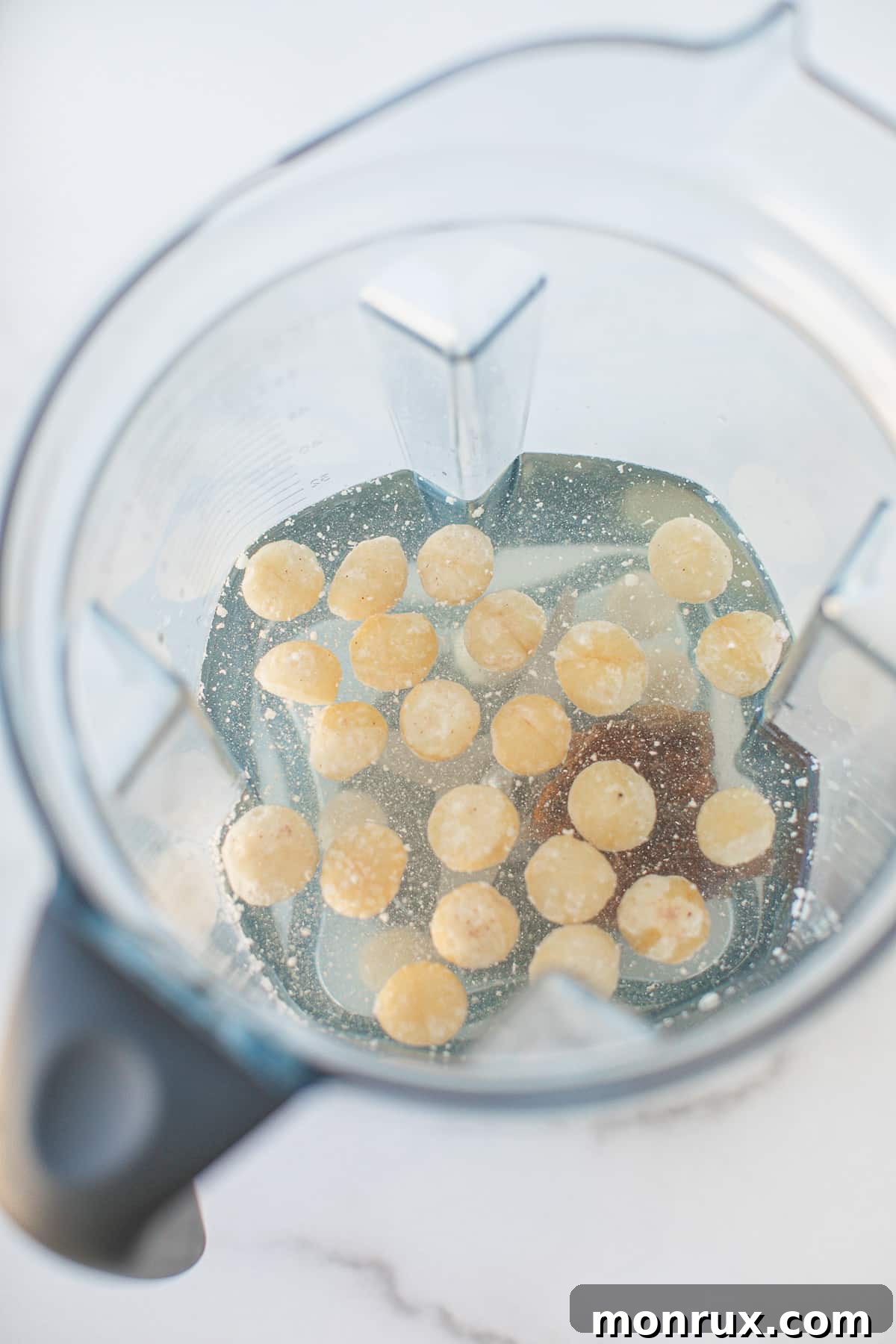 Raw macadamia nuts and filtered water being added into a high-speed blender pitcher.